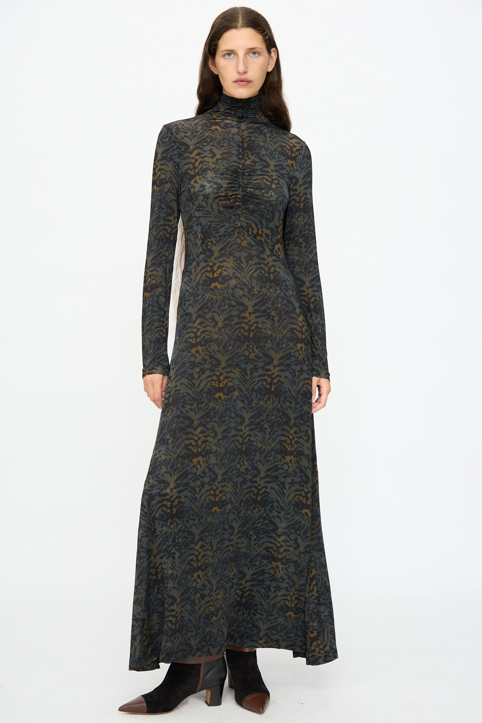 A woman stands against a white background wearing the Ulla Johnson Koa Dress in Desert Jasper, a slim-fit maxi dress, paired with black ankle boots.