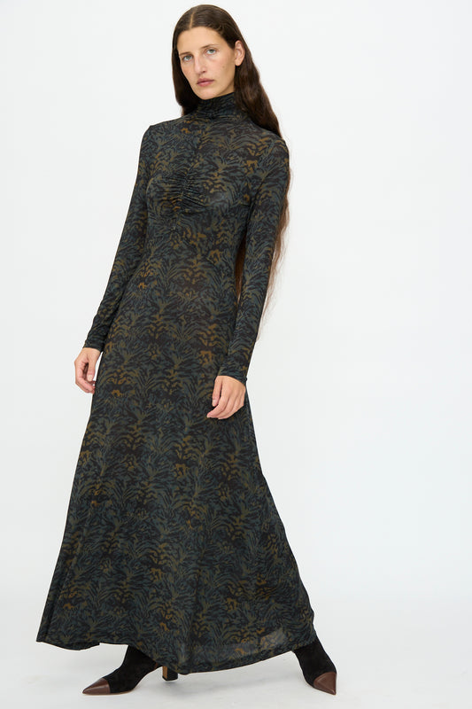 A woman models the Ulla Johnson Koa Dress in Desert Jasper, a slim fit maxi with long sleeves, high neck, and ikat animal print, set against a plain white background.