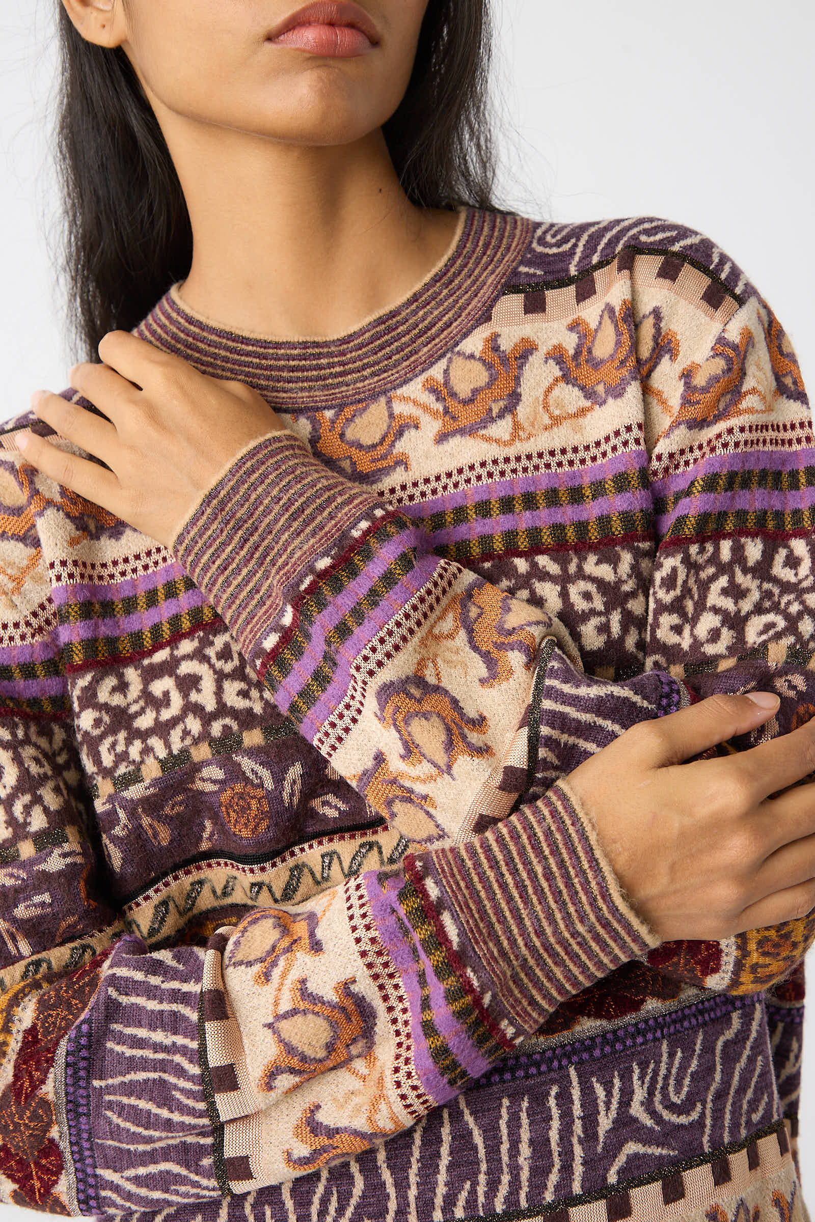 A woman with long hair, clad in the Ulla Johnson Lara Pullover in Woodland adorned with Fair Isle motifs and vibrant colors, stands with her arms crossed.