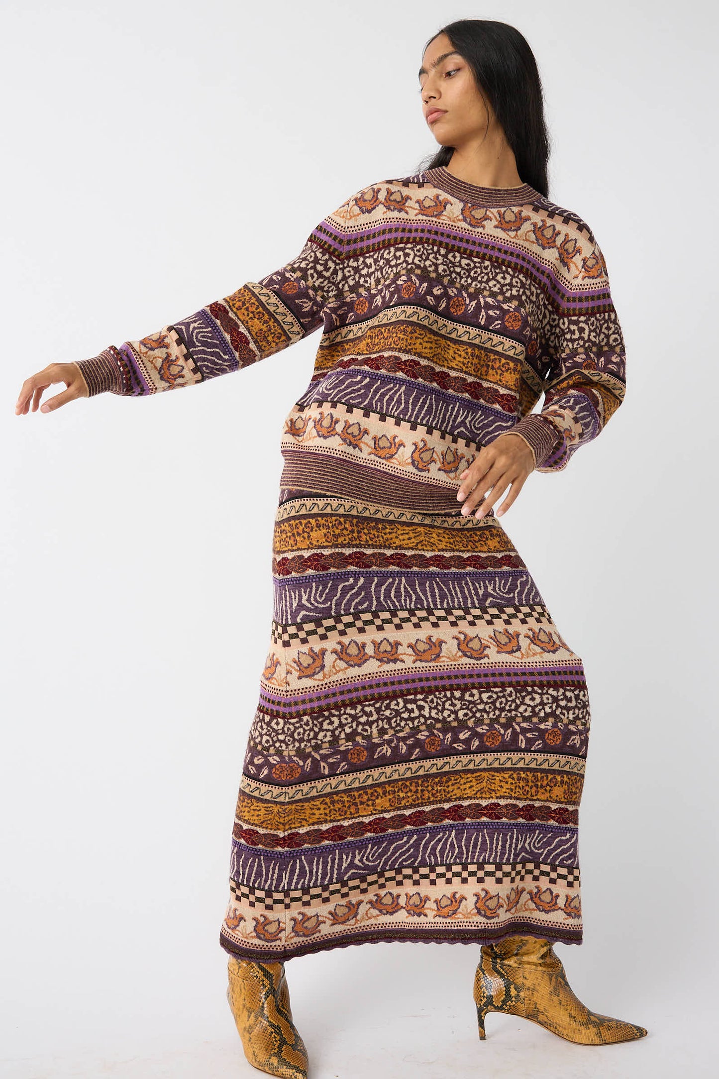 A person in the Lara Pullover in Woodland by Ulla Johnson, a long-sleeve pullover with multicolored Fair Isle motifs, poses with one arm slightly raised and the other near their torso, wearing pointed-toe shoes.