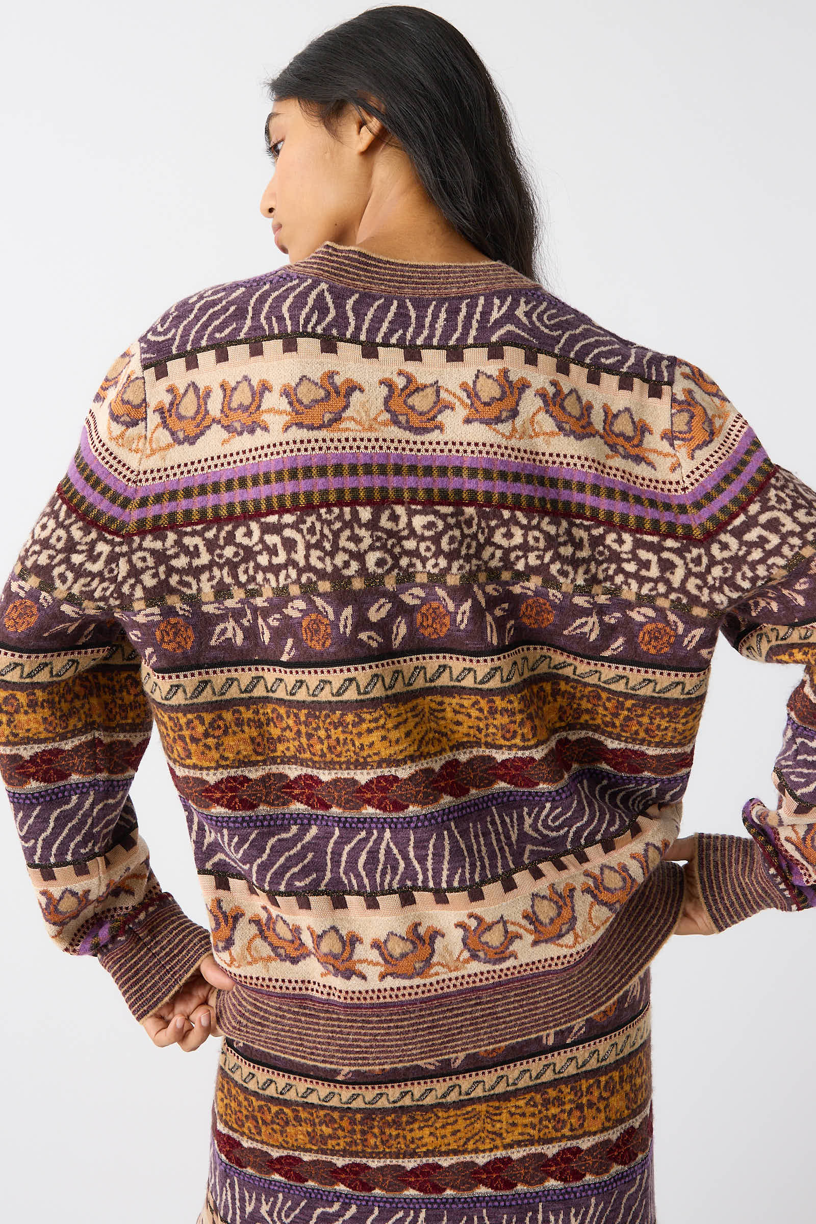 A person with long dark hair shows the back of the Lara Pullover in Woodland, a colorful, patterned sweater by Ulla Johnson crafted with mid-weight plush yarn. The design features various shades of purple, brown, and yellow in intricate Fair Isle motifs.