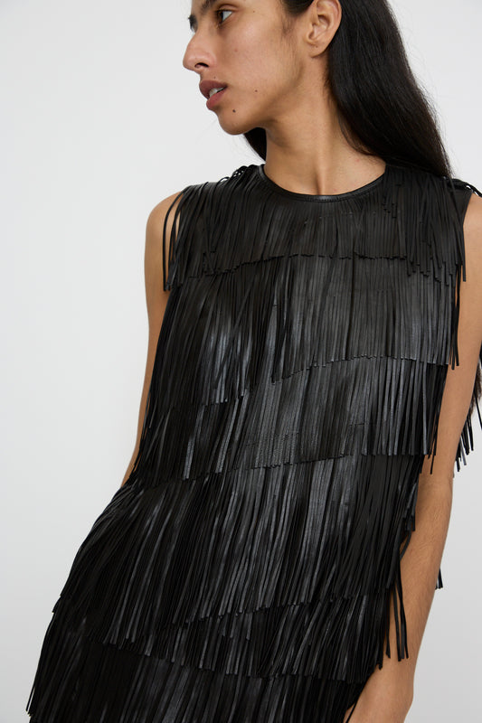 A person stands against a plain background, wearing the Leonie Top in Noir by Ulla Johnson, with its sleeveless design and raw-edge fringe details.