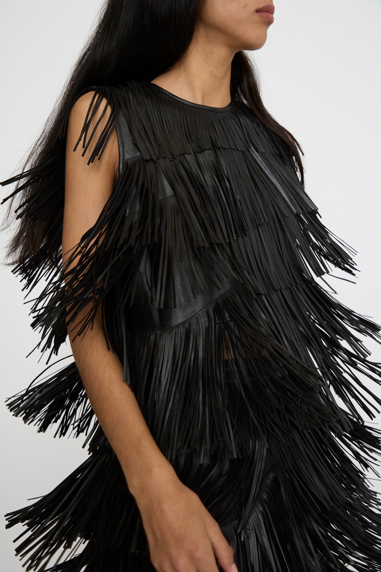 Close-up of a person wearing the Ulla Johnson Leonie Top in Noir, featuring raw-edge fringe, with long straight dark hair standing against a plain background.