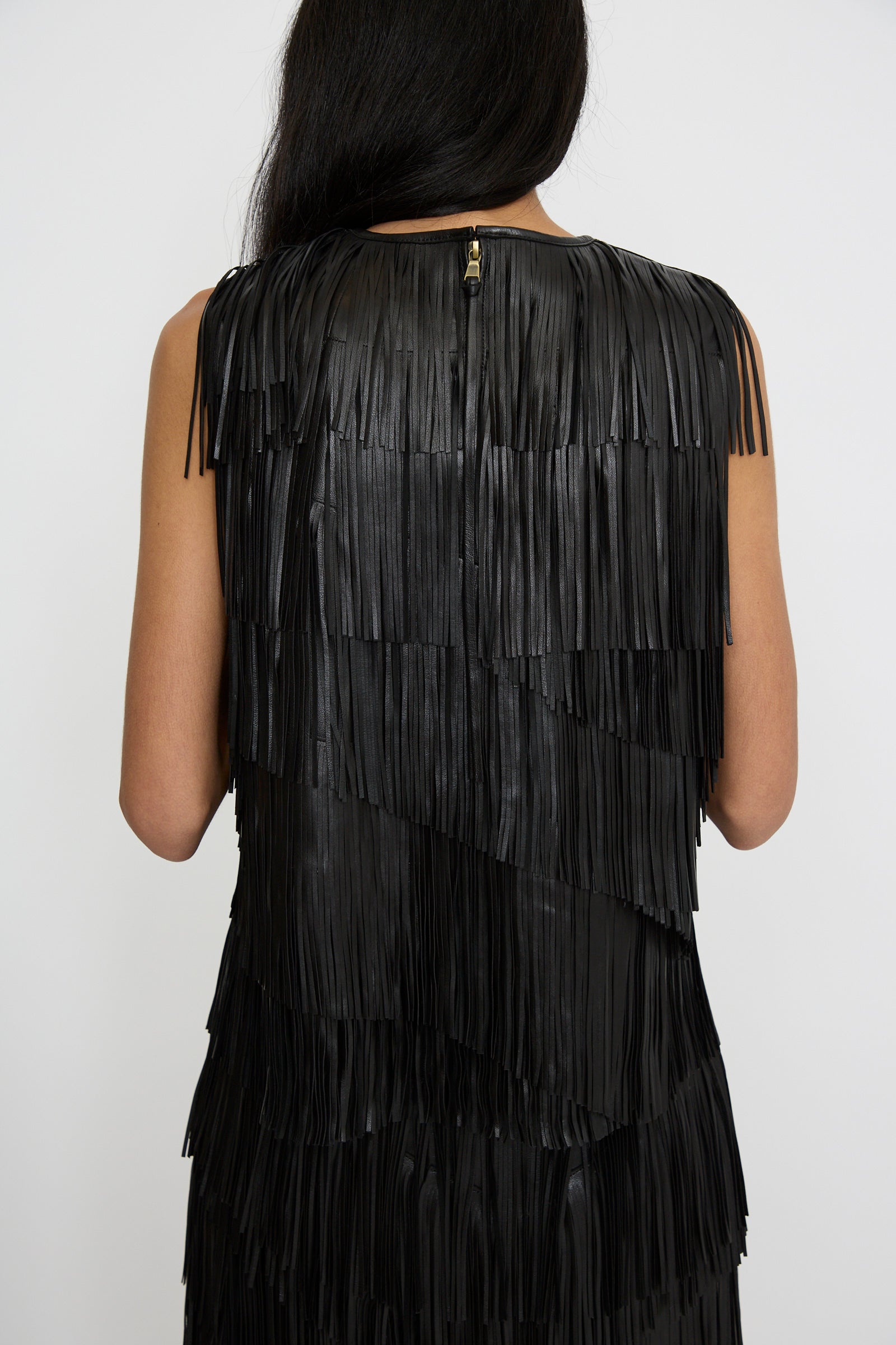 A person wearing the Leonie Top in Noir by Ulla Johnson showcases their long dark hair and sleeveless top, featuring a black raw-edge fringe, as seen from the back.