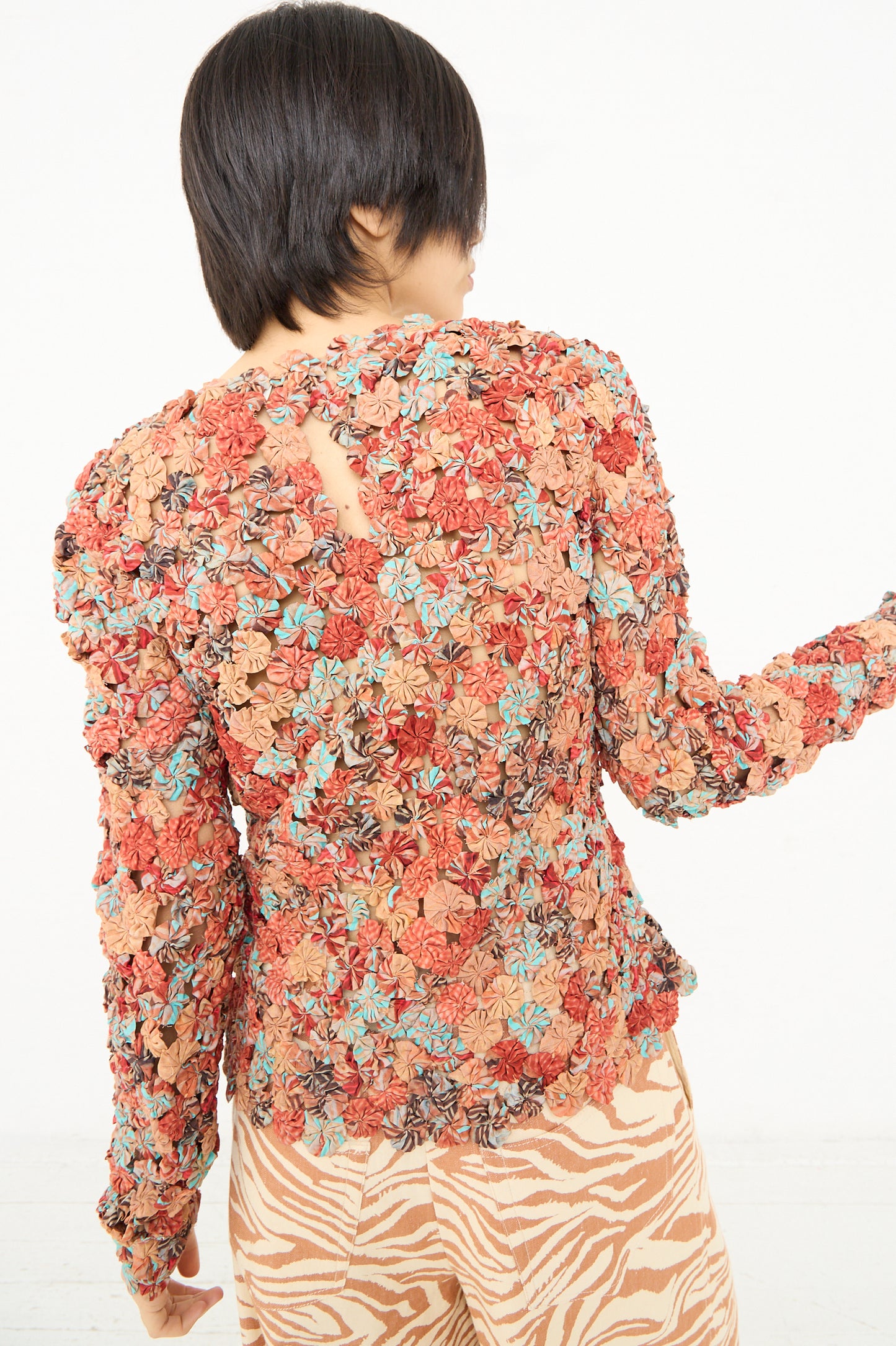 Woman posing with her back to the camera showcasing a Ulla Johnson Magdalene Top in Mariposa, featuring a floral-patterned, long sleeve top with a cut-out detail and silk rosettes.