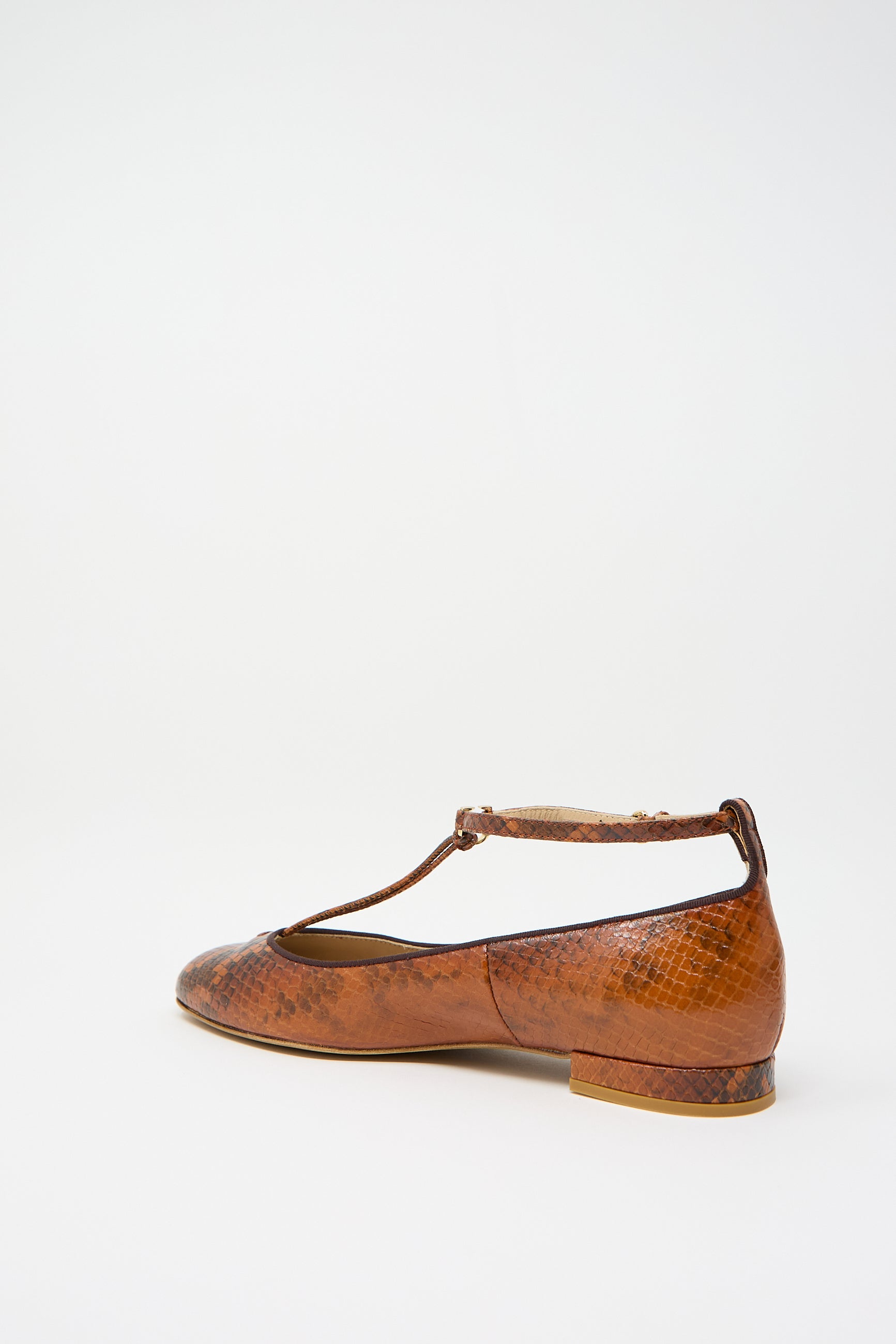 A Mary Jane in Rust Copper by Ulla Johnson featuring a brown flat design, adjustable ankle strap, and snakeskin pattern, viewed from the side against a white background.