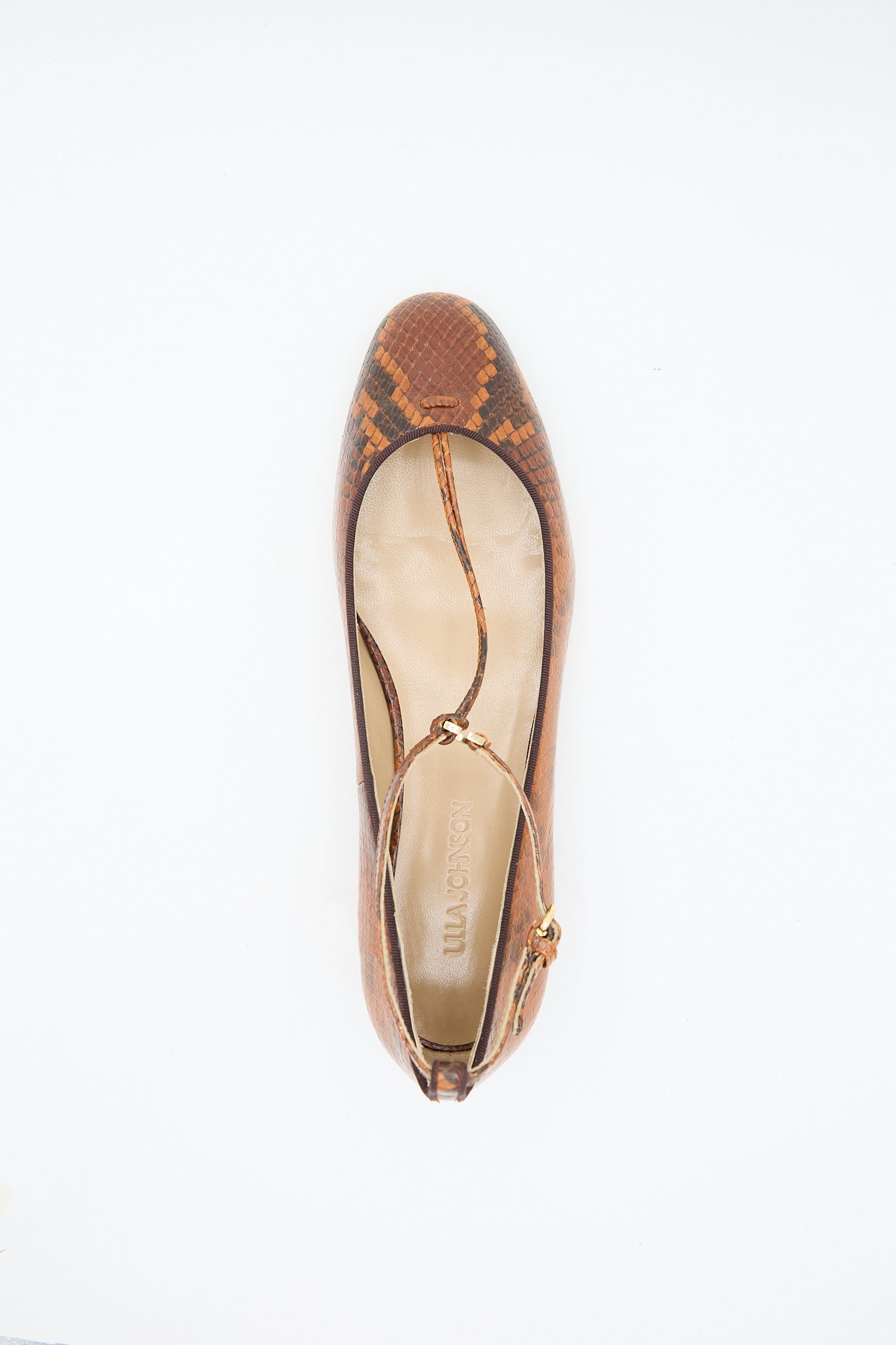 A single "Mary Jane in Rust Copper" flat shoe by Ulla Johnson, featuring a snakeskin pattern and an adjustable ankle strap, viewed from above on a white background.