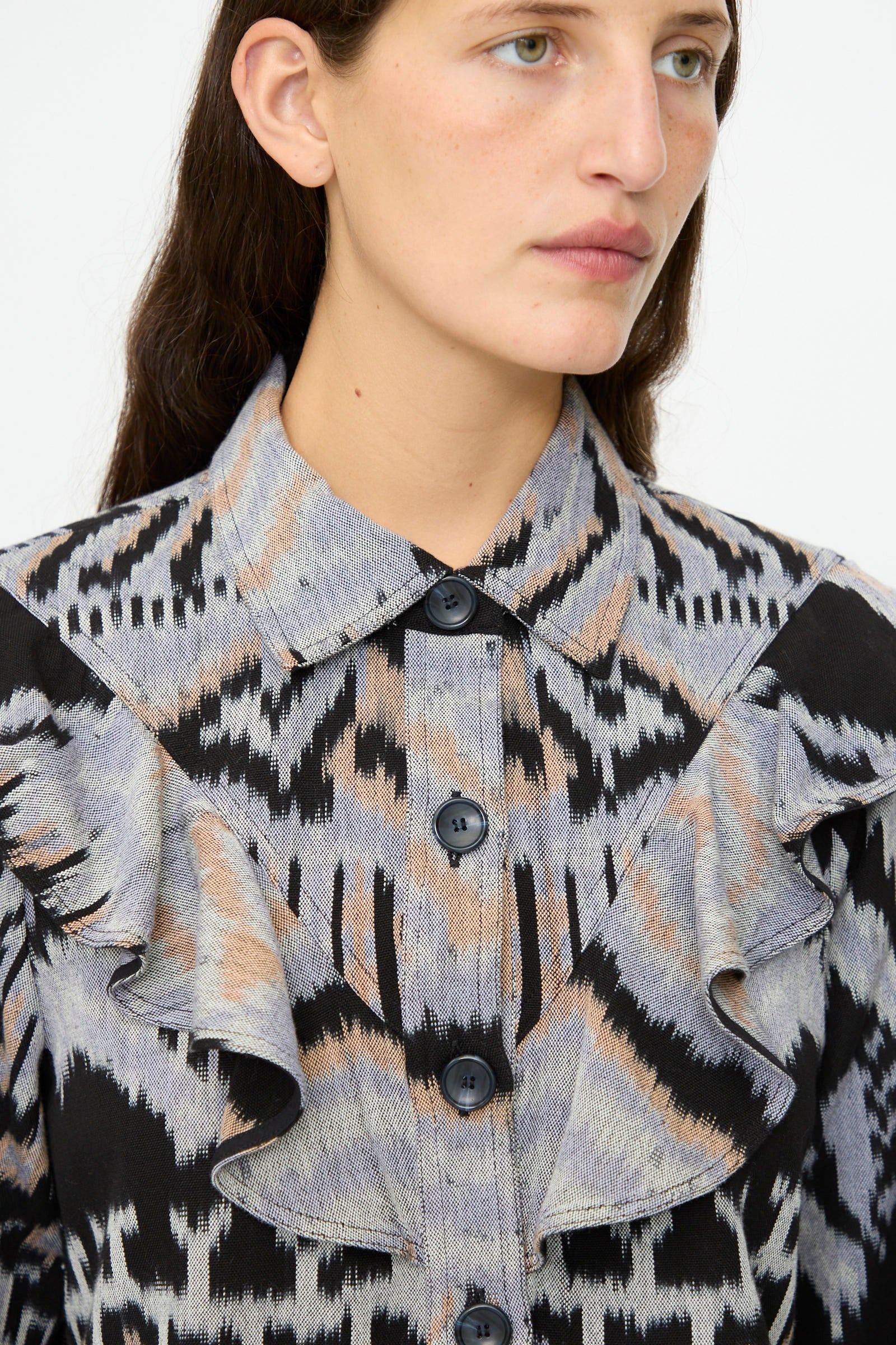 A woman wearing the Ulla Johnson Mathilde Blouse in Tigereye, a long sleeve cotton top with a bold black, grey, and beige abstract print and ruffle details on the front.