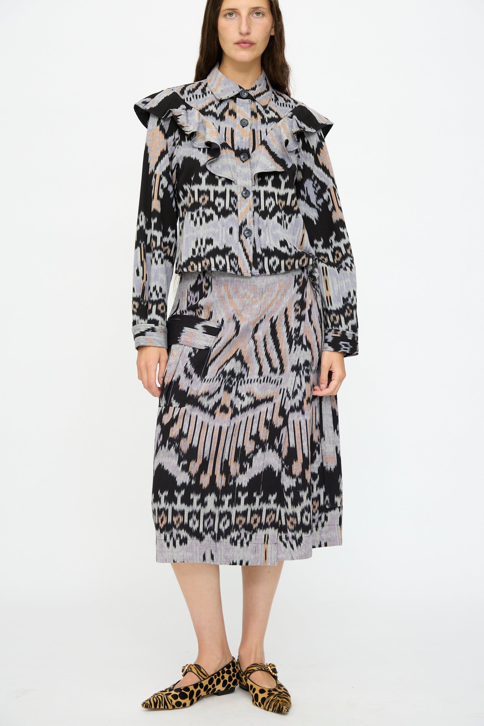 A woman wears a patterned blouse, the Ulla Johnson Mila Pencil Skirt in Tigereye, and leopard-print pointed flats against a plain white background.