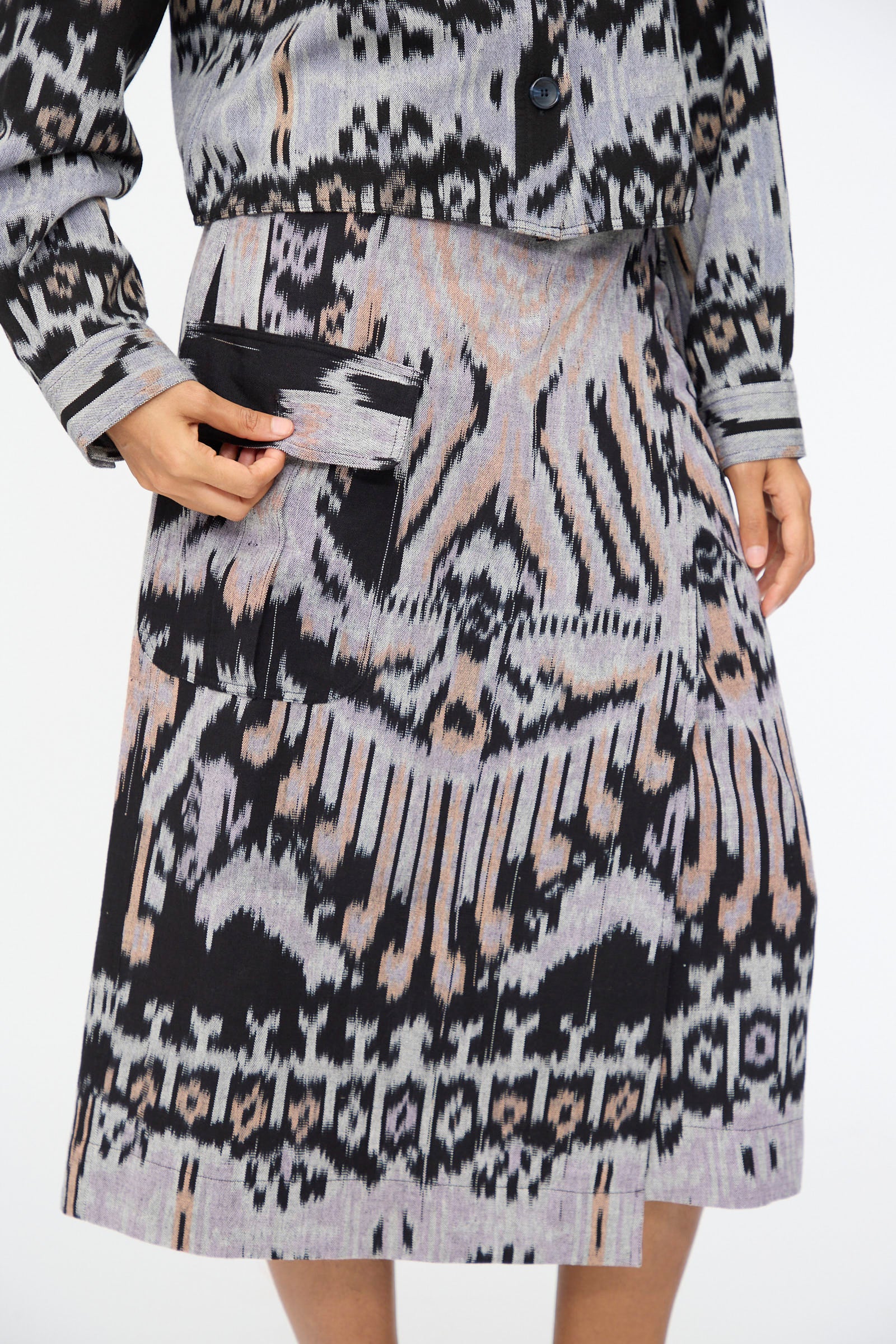 A person wearing the Ulla Johnson Mila Pencil Skirt in Tigereye with ikat motifs, styled with a matching jacket and their hand placed in the skirt’s large front pocket.