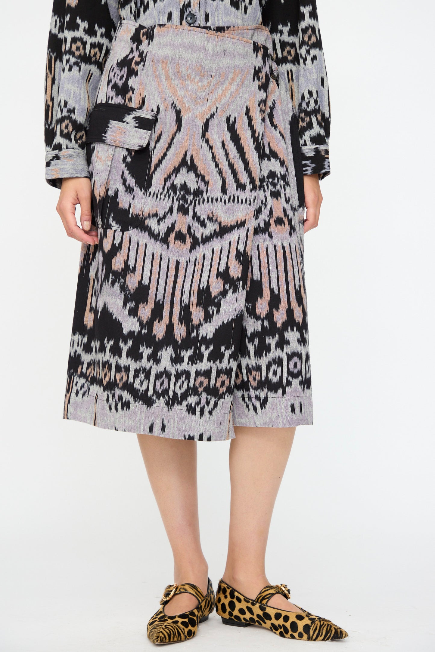 A person wears the Ulla Johnson Mila Pencil Skirt in Tigereye, paired with a matching top and leopard print flats, standing against a white background.