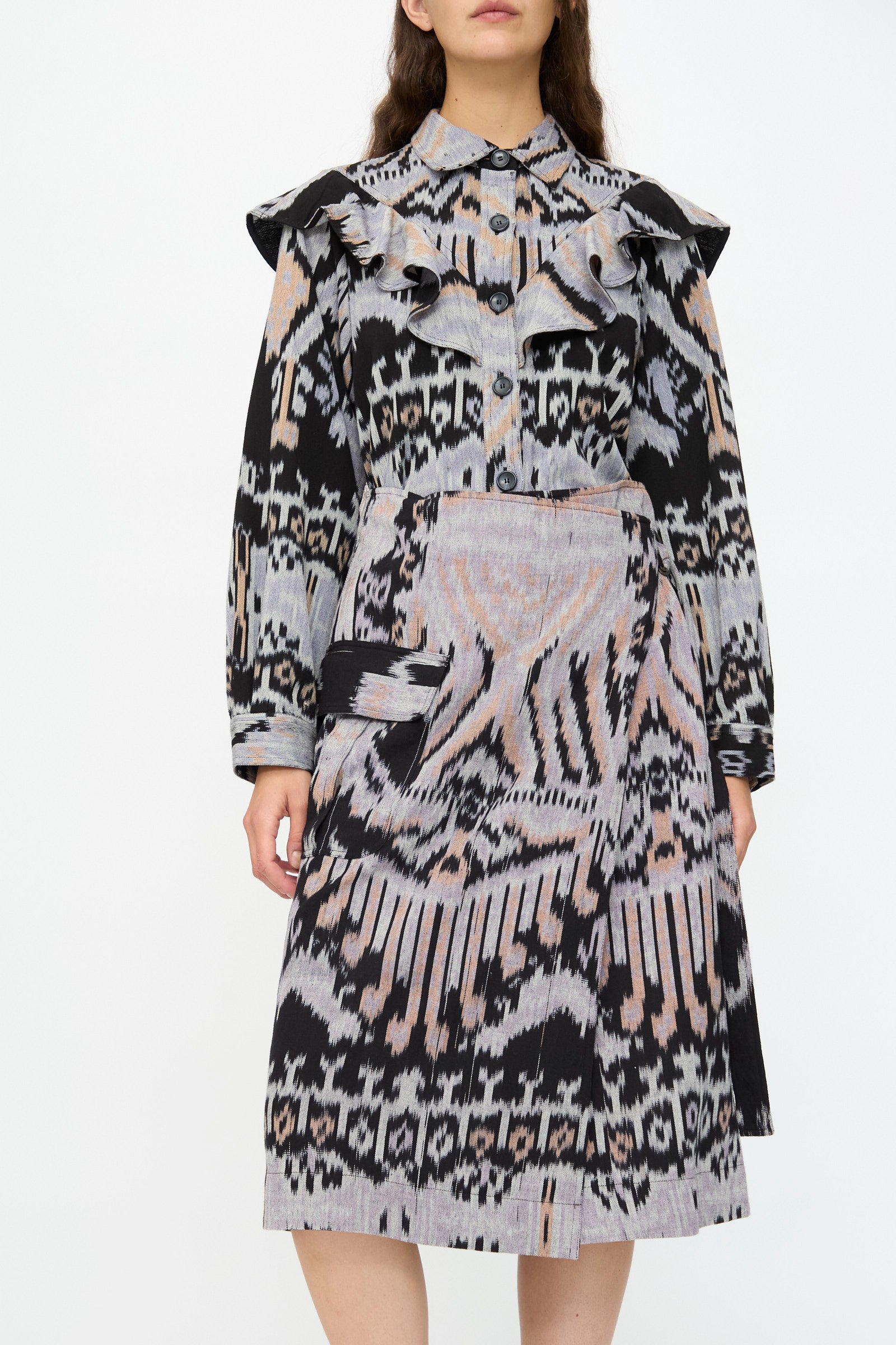 A person stands against a plain background wearing the Ulla Johnson Mila Pencil Skirt in Tigereye, featuring a black, white, and beige abstract geometric pattern.