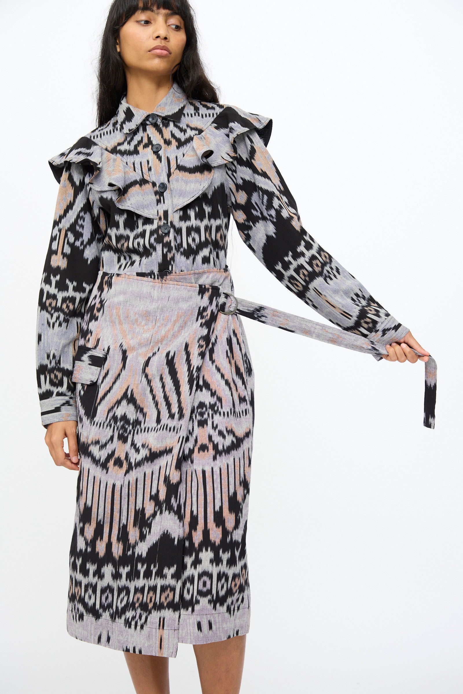 A woman adjusts the belt of her Mila Pencil Skirt in Tigereye by Ulla Johnson, a hand-loomed cotton skirt featuring geometric and abstract prints in black, grey, and pink hues.