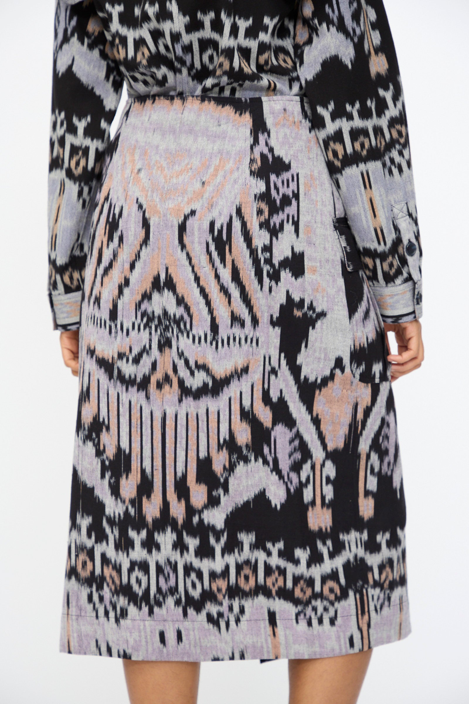 A person is seen from the back wearing the Ulla Johnson Mila Pencil Skirt in Tigereye, a hand-loomed cotton midi skirt with geometric and abstract designs and subtle ikat motifs in black, grey, and beige.