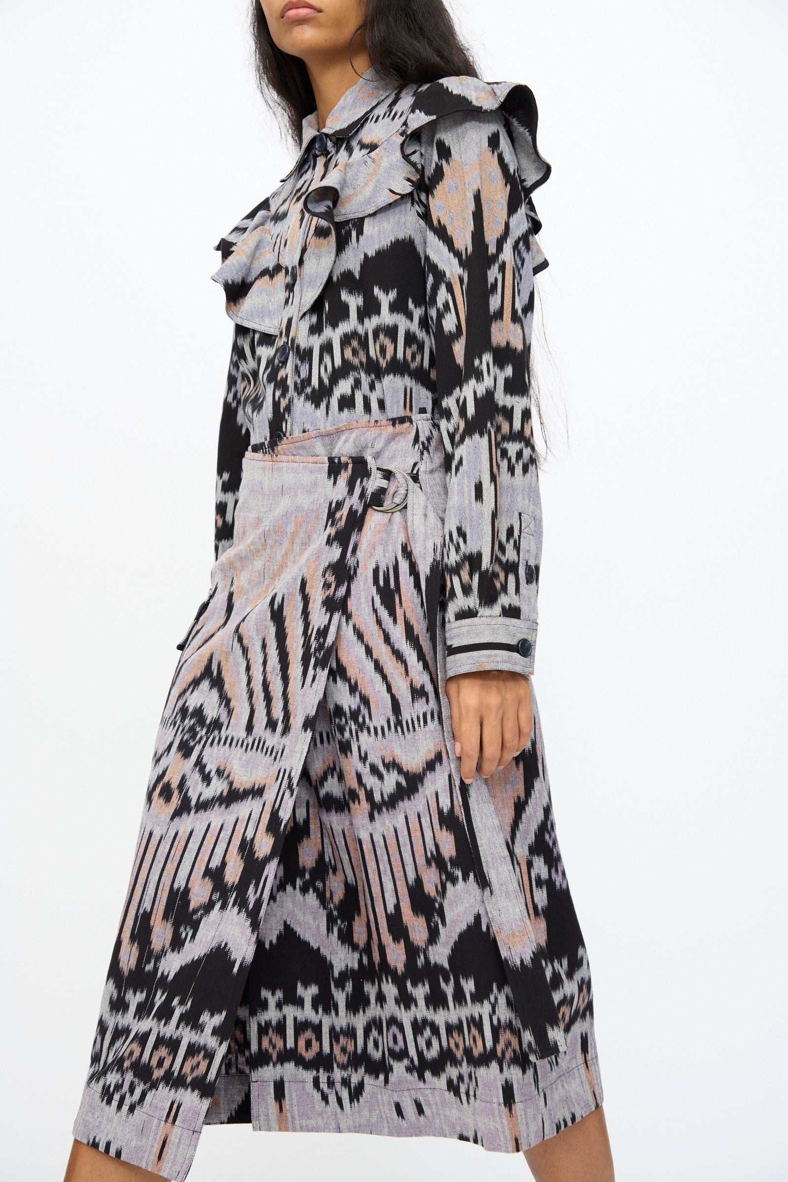 A woman wears the Mila Pencil Skirt in Tigereye by Ulla Johnson, featuring black, gray, and pink abstract ikat-inspired patterns with ruffled details at the waist.