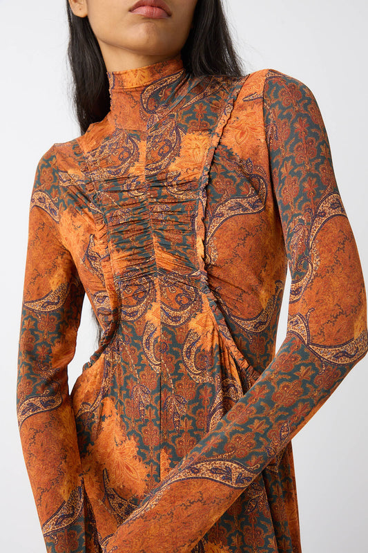 A person wearing the Ulla Johnson Oriana Dress in Amber, a long-sleeve, fitted turtleneck dress featuring an intricate and vibrant orange and green paisley print.