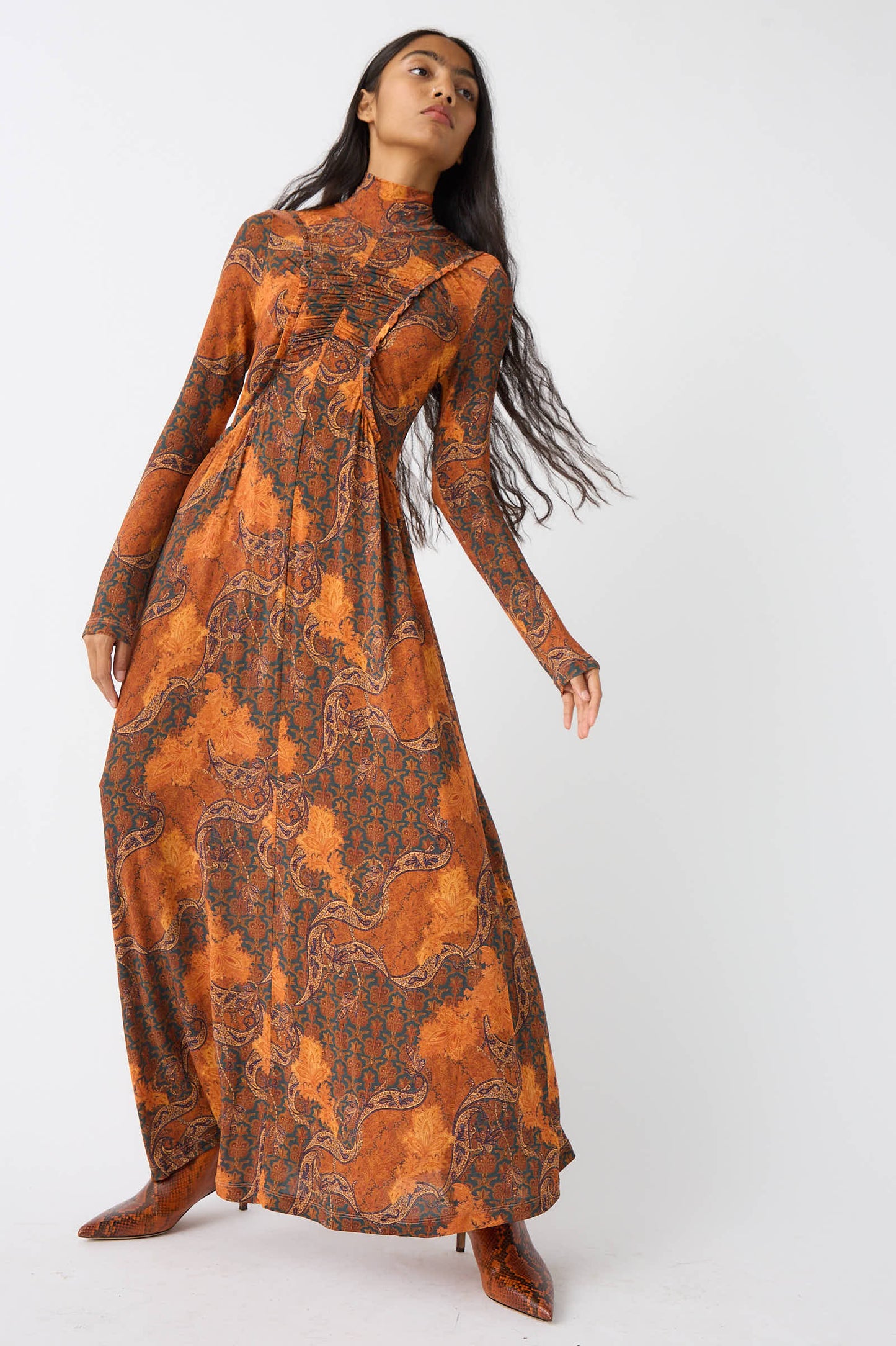 A person with long hair wearing the Oriana Dress in Amber by Ulla Johnson, featuring a vibrant paisley print, poses against a plain white background.