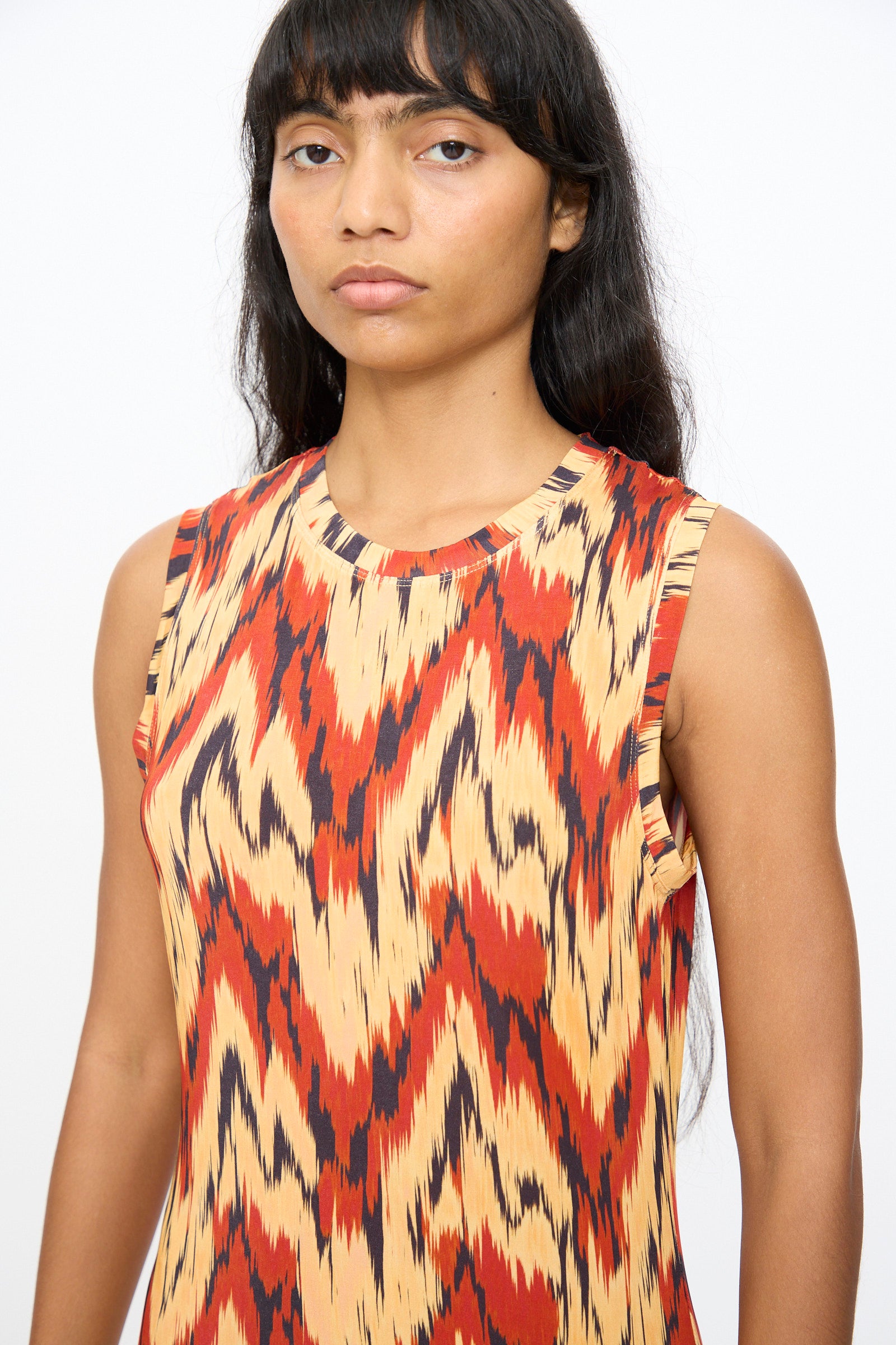 A woman with long dark hair wears the Ulla Johnson Orla Dress in Carnelian, featuring a bold zigzag pattern, standing against a plain white background.
