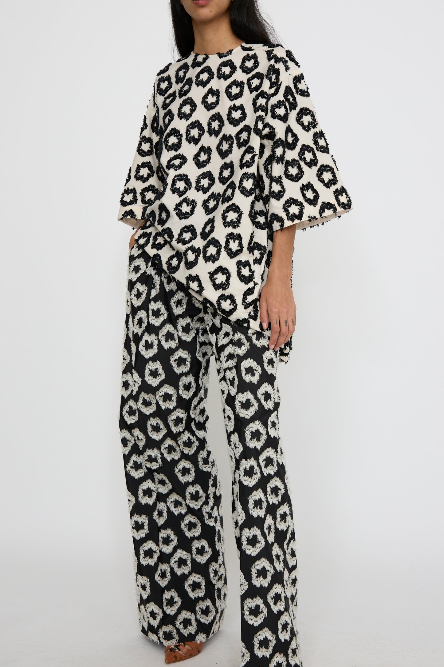 A person dressed in the Remy Tunic in Lunar by Ulla Johnson, featuring a matching black and white graphic pattern with wide sleeves and loose pants, crafted from a comfortable cotton blend against a white background. 