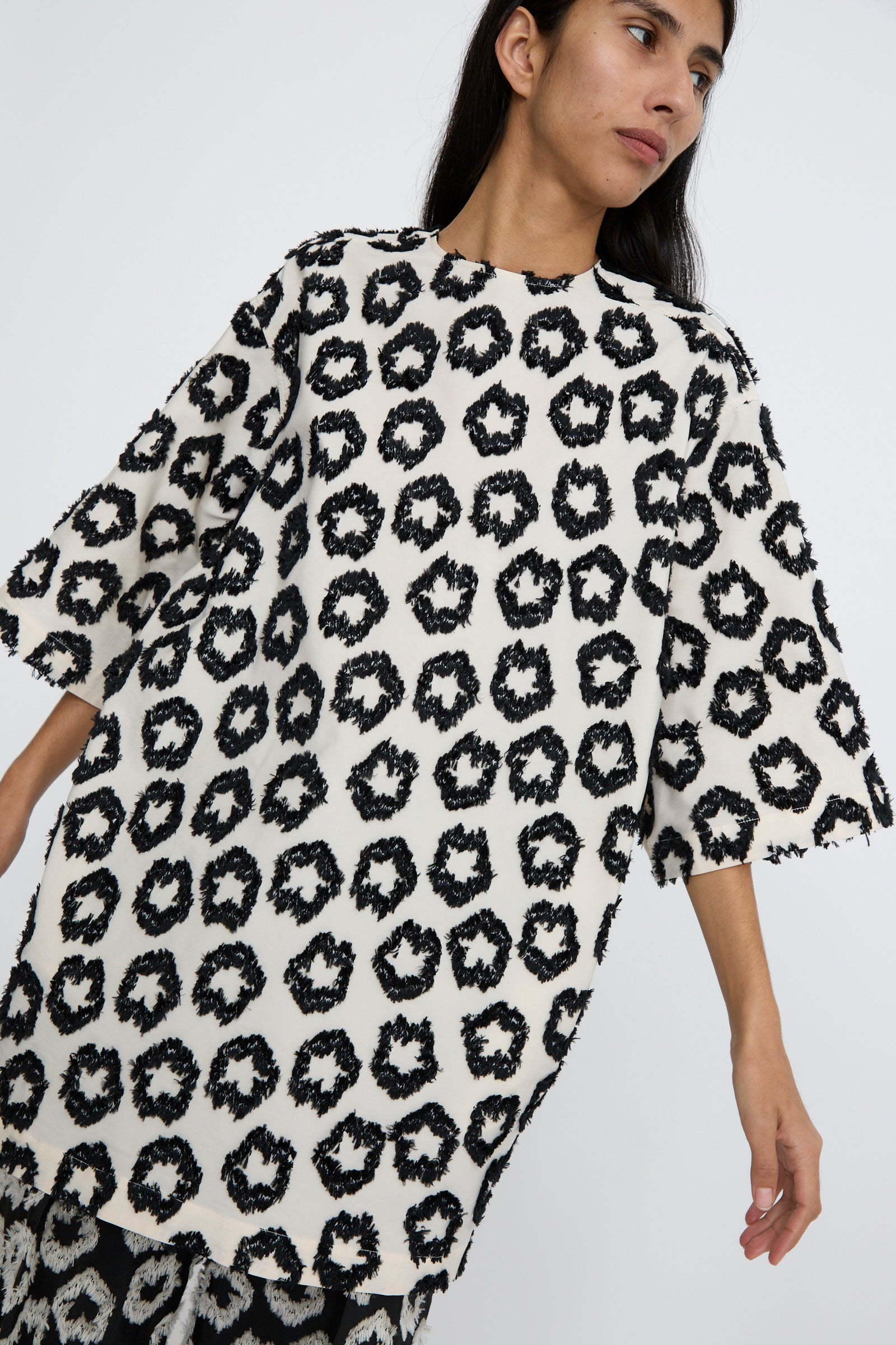 A person stands against a plain background and looks to the left, wearing the Remy Tunic in Lunar by Ulla Johnson, featuring an oversized fit with a graphic pattern. 