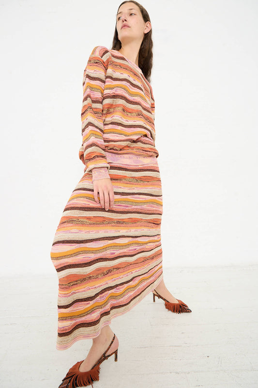 A person wearing a patterned, long-sleeve top and matching jacquard knit Ulla Johnson Rosen Skirt in Sunset with wavy stripes poses against a plain white background. They are also wearing brown heeled sandals with fringe detail.