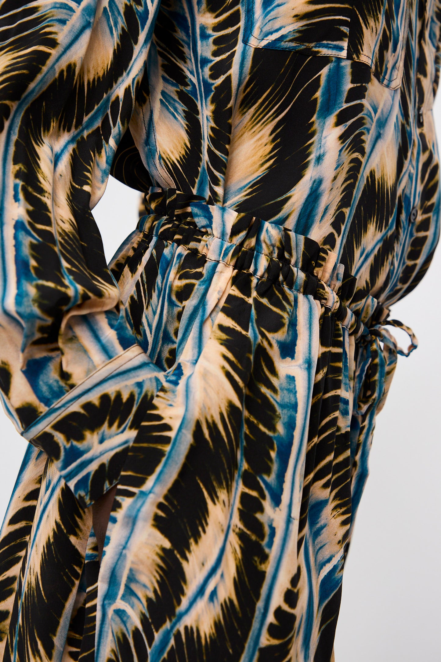 Close-up of the Shibori Wave Printed Sawyer Pant in River by Ulla Johnson, featuring a blue, black, and beige abstract pattern with gathered waist detail, textured fabric, and pocket—ideal for pairing with oversized pants.