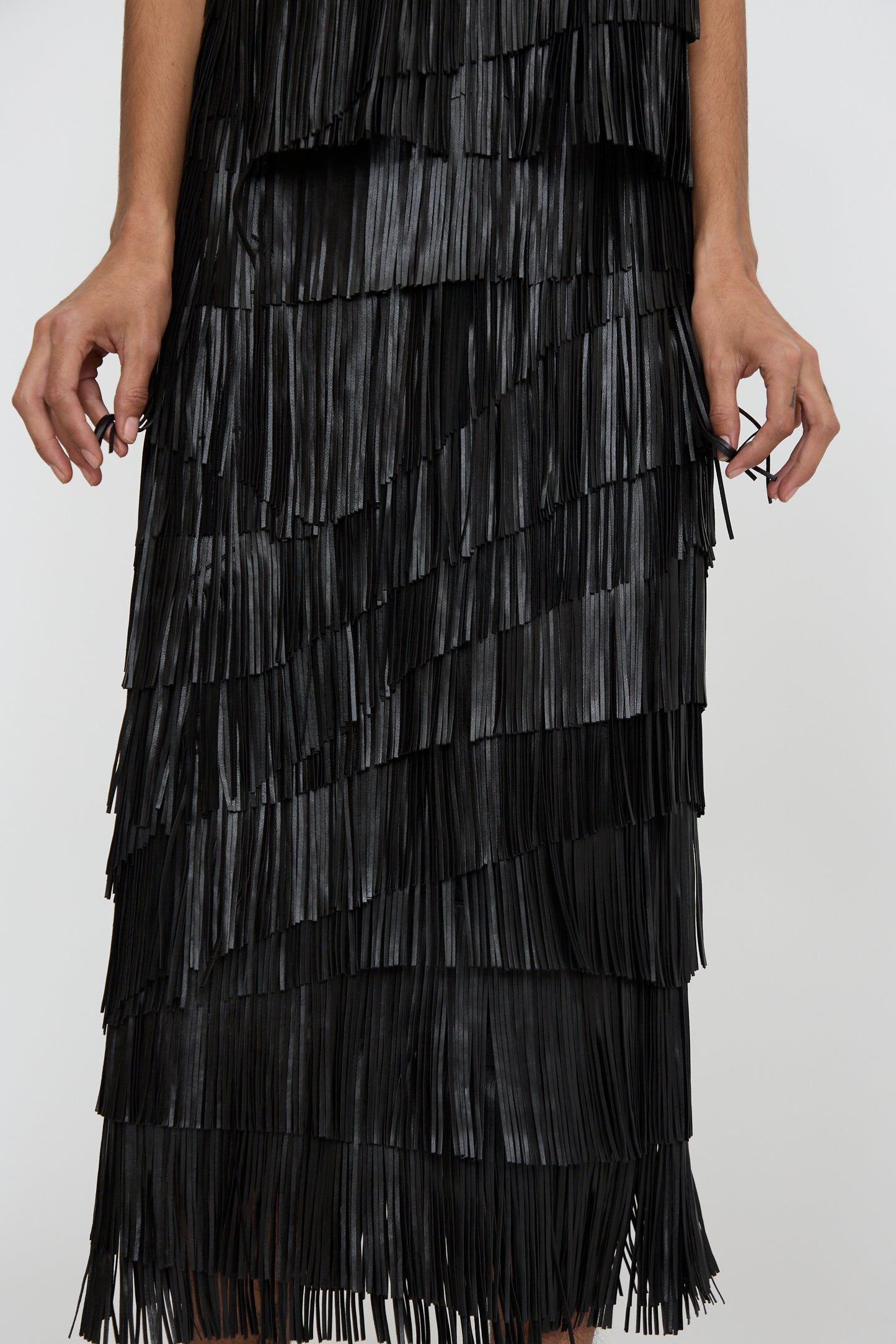 A person is show below the torso wearing the Therese Skirt in Noir by Ulla Johnson, featuring layered fringe, against a white background.