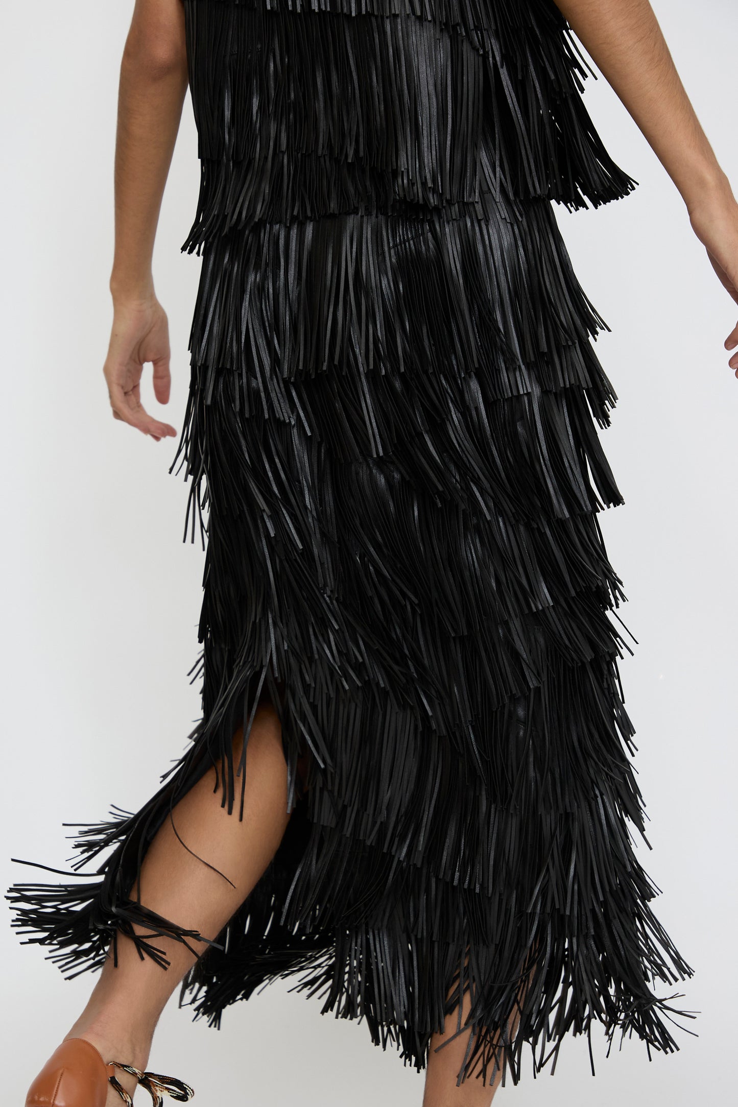 A person wearing the Ulla Johnson Therese Skirt in Noir moves gracefully against a plain background, while the layered fringe sways with each step.