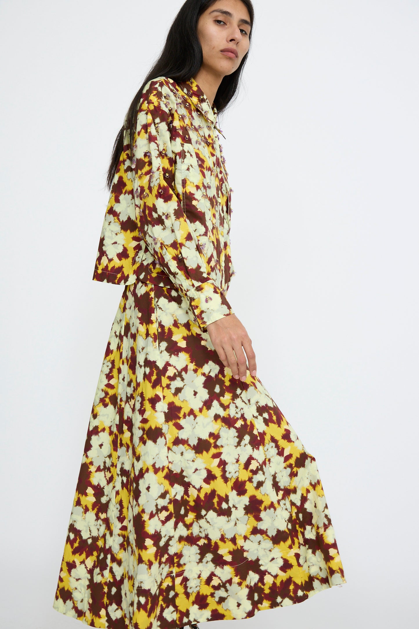 A person is dressed in the Vianne Skirt by Ulla Johnson, crafted from soft cotton poplin and featuring yellow and brown floral patterns on a simple background.