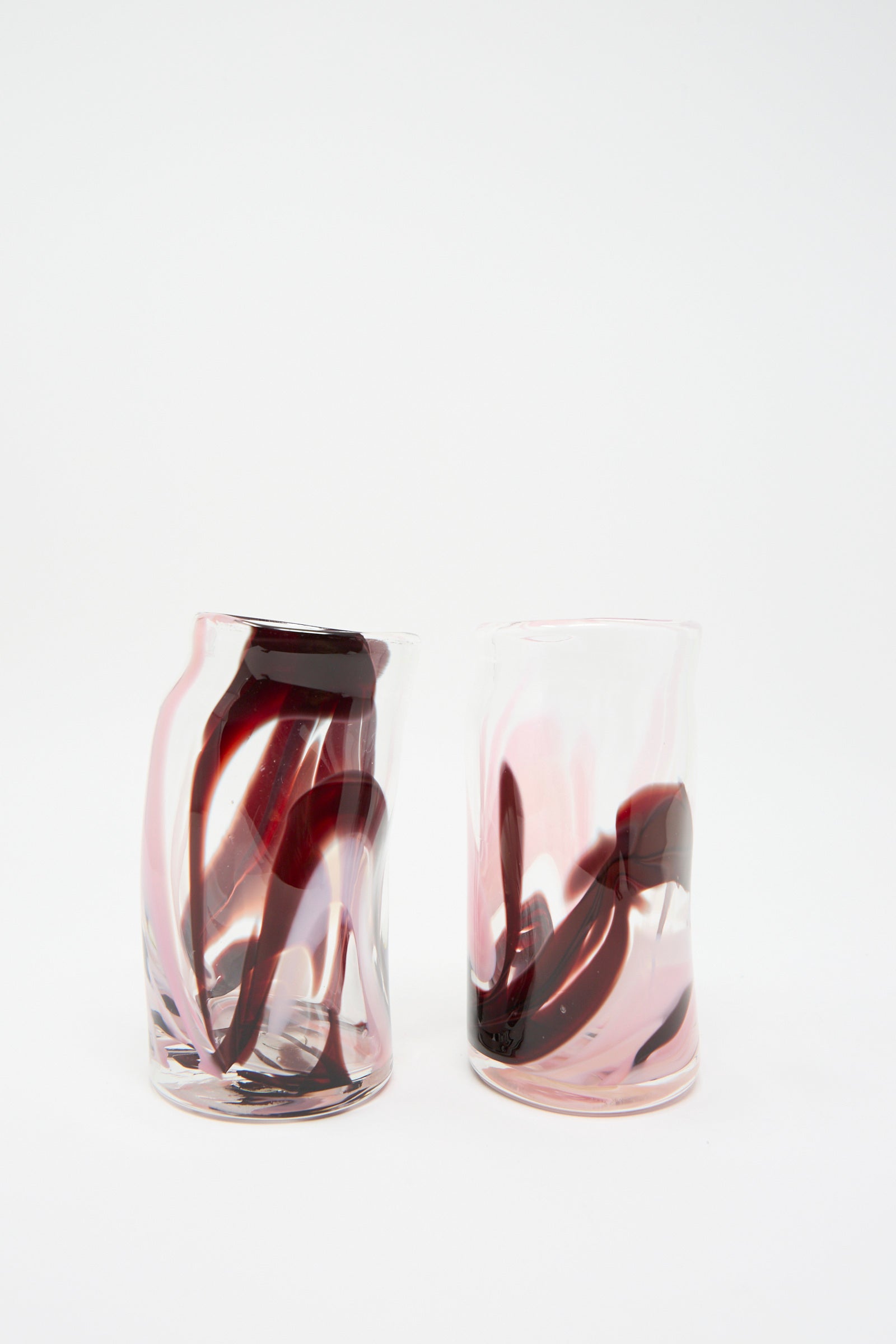 The Gamay Crinkle Cup by Upstate, featuring two handblown glass tumblers with vibrant red and pink swirling patterns, effortlessly captures attention against a plain white background. Their elegant design suggests a wavy shape, adding an artistic touch to these highball glasses.