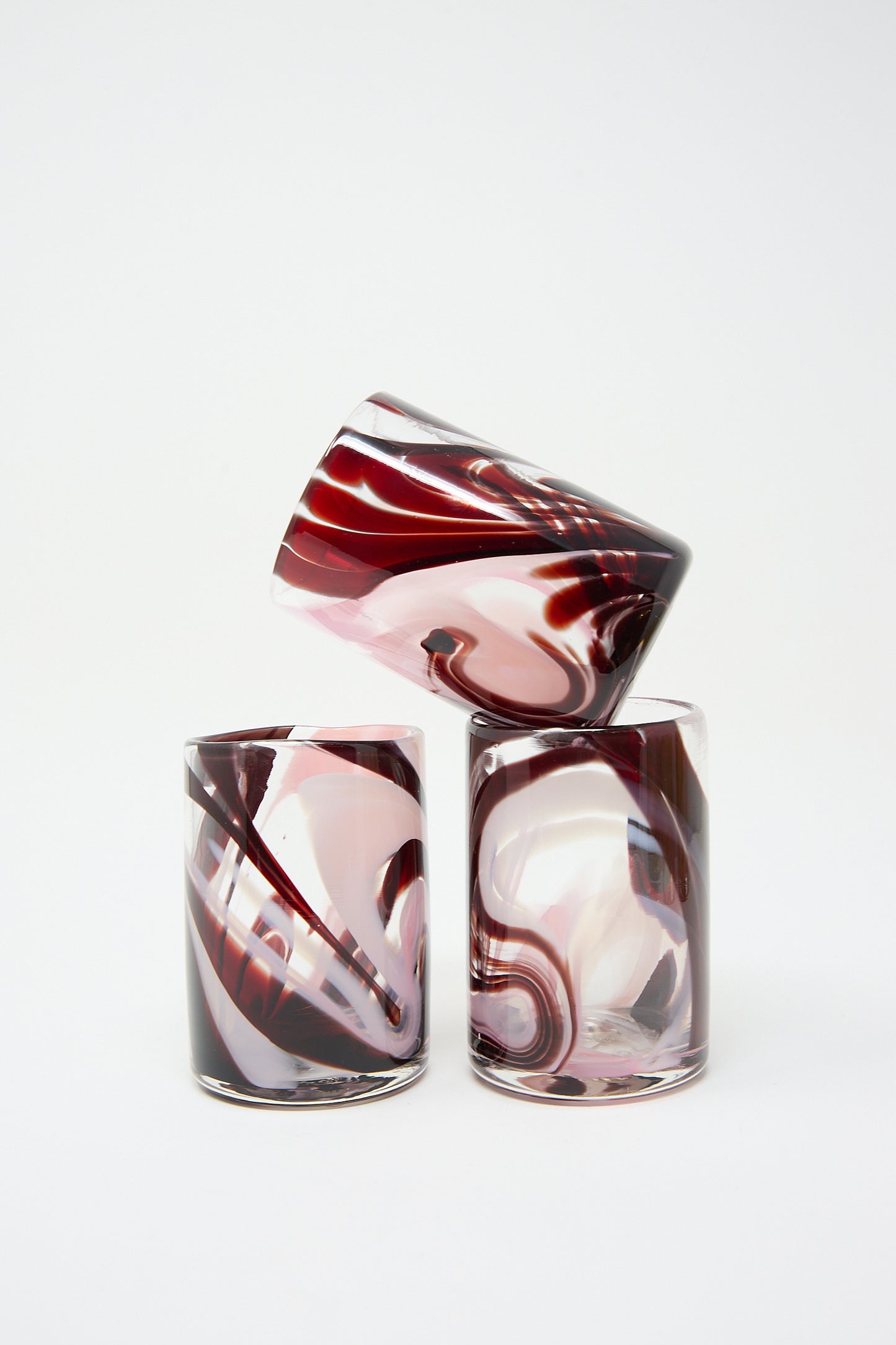 Three Gamay Cups crafted by artisans in NYC, featuring unique abstract swirling red and white patterns, one tipped on its side. (Brand: Upstate)