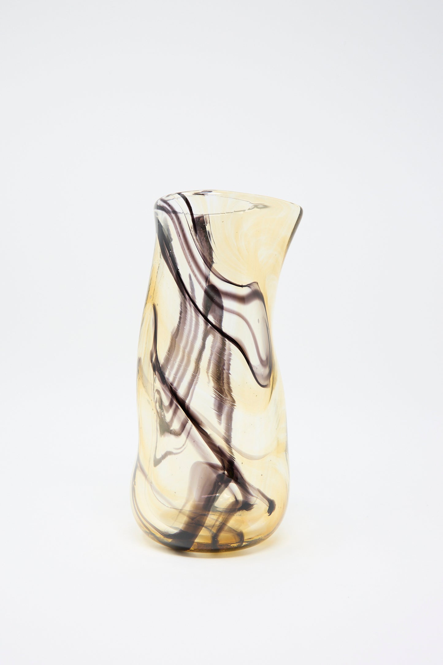 A tall, asymmetrical glass carafe from Upstate, known as the Hand Blown Fumé Carafe in Smoke and Tobacco, features swirling smoke and tobacco patterns on a white background.