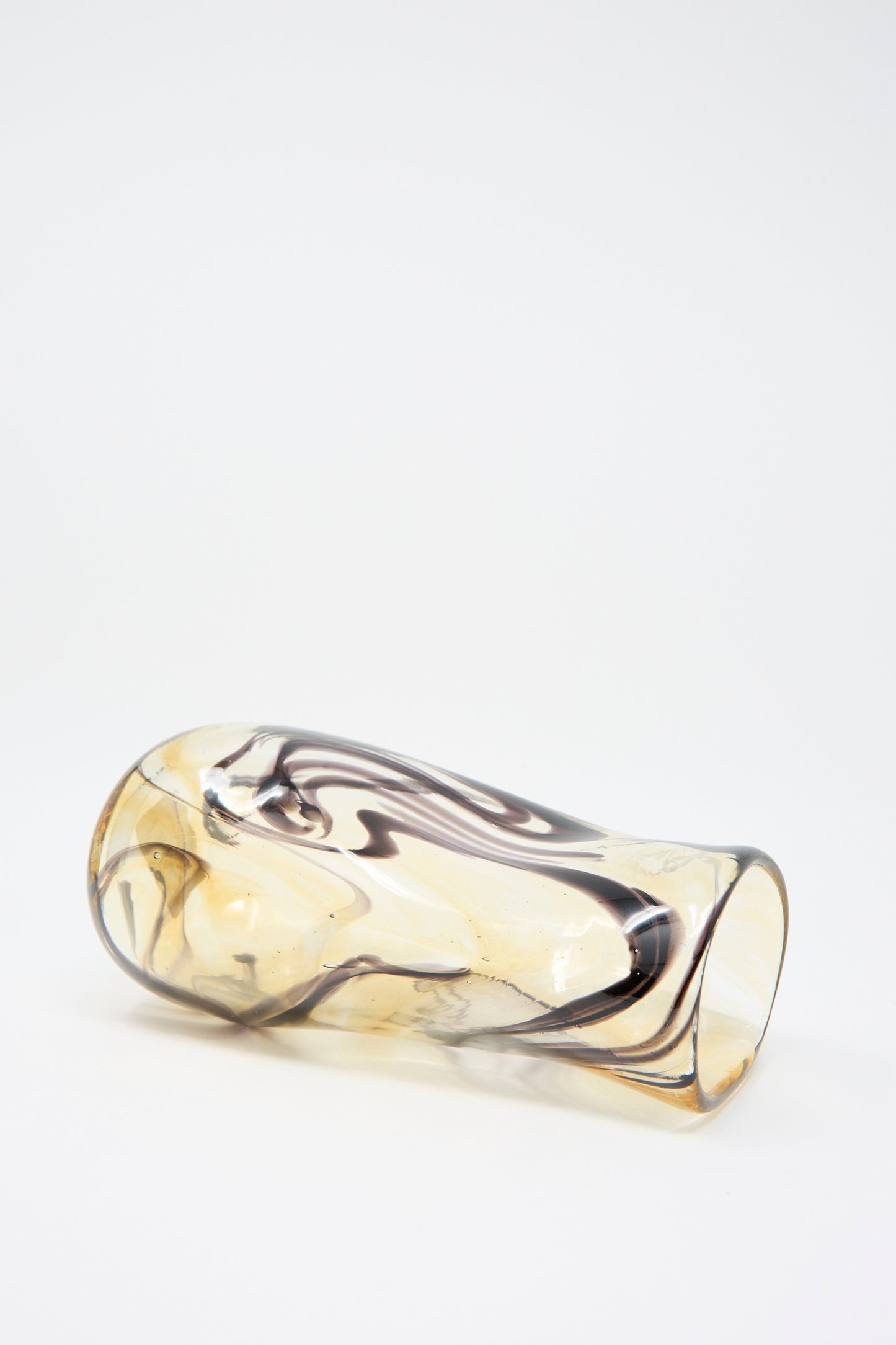 A Hand Blown Fumé Carafe in Smoke and Tobacco by Upstate lies on its side against a plain background, showcasing abstract color swirls of brown.