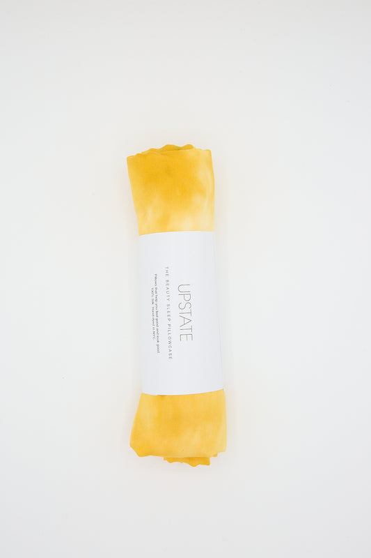 A rolled-up Marigold hand-dyed silk pillowcase with a white label against a white background by Upstate.