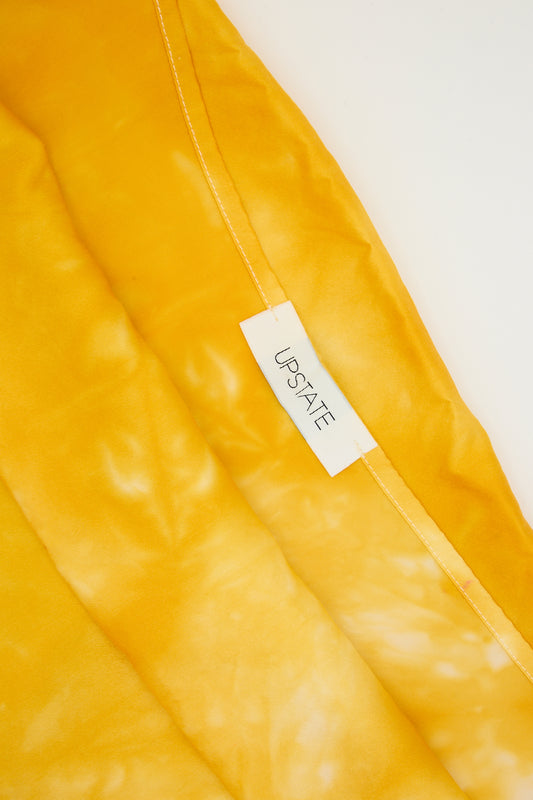 A close-up of a marigold silk pillowcase with a clothing label that reads "Upstate".