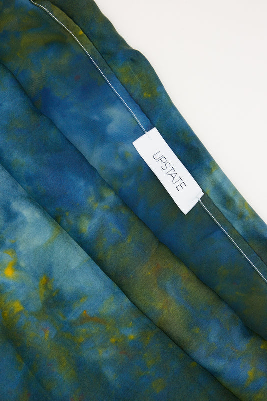 A close-up of a Silk Pillowcase in Peacock from Upstate with a peacock-blue and green tie-dye pattern on 100% Silk Charmeuse and a white size tag labeled "us size.