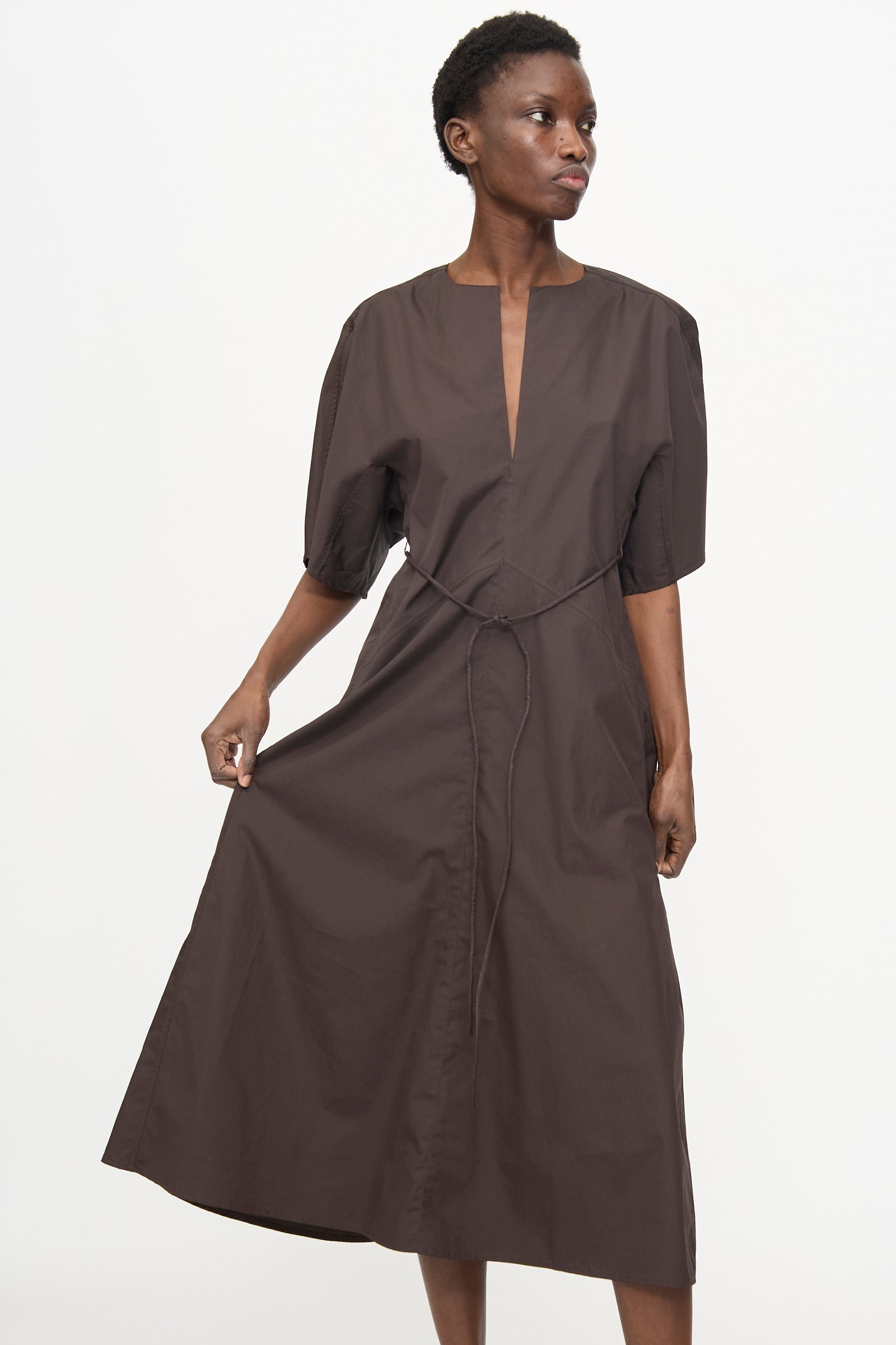 A person wearing the Veronique Leroy Belted Kimono Dress in Choco, featuring a relaxed fit, knee-length cut, short sleeves, and V-neckline, stands against a plain white background.