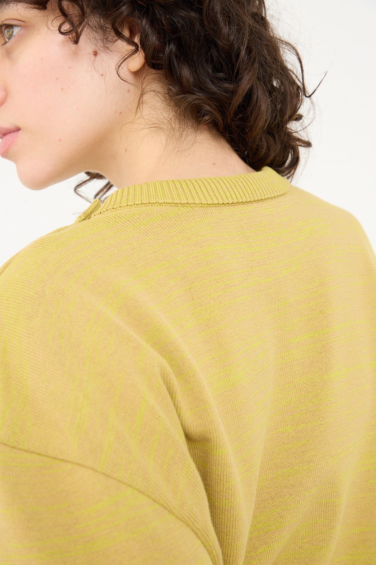 The back of a woman, slightly covered by her Veronique Leroy Cotton Boxy Sweater in Curry.