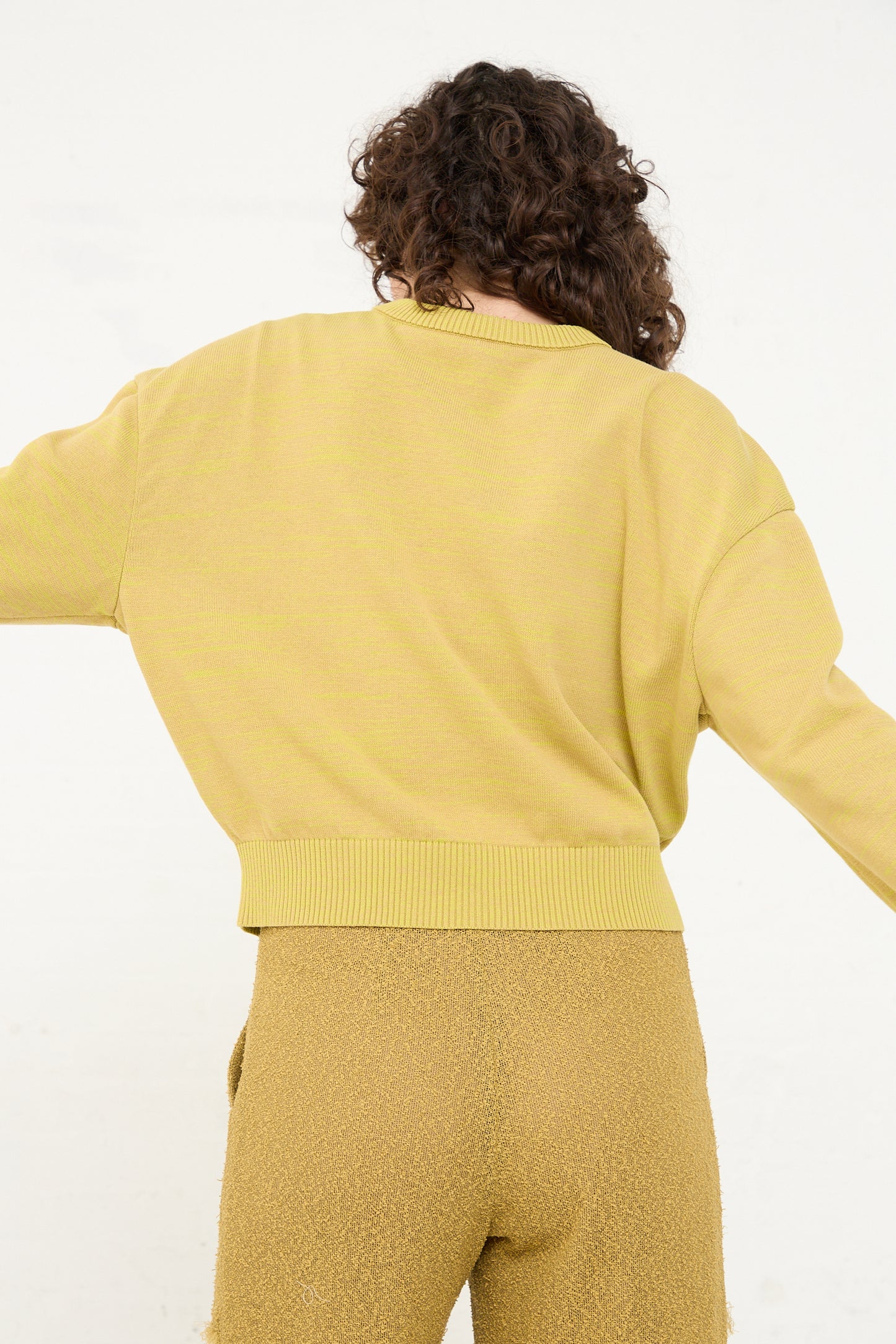 The back of a woman wearing a yellow knit Cotton Boxy Sweater in Curry by Veronique Leroy.