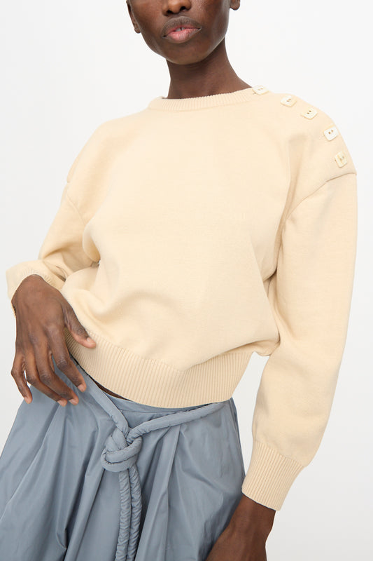 A person wearing the Veronique Leroy Button Shoulder Boxy Sweater in Cream paired with a light blue belted skirt, standing against a plain background.