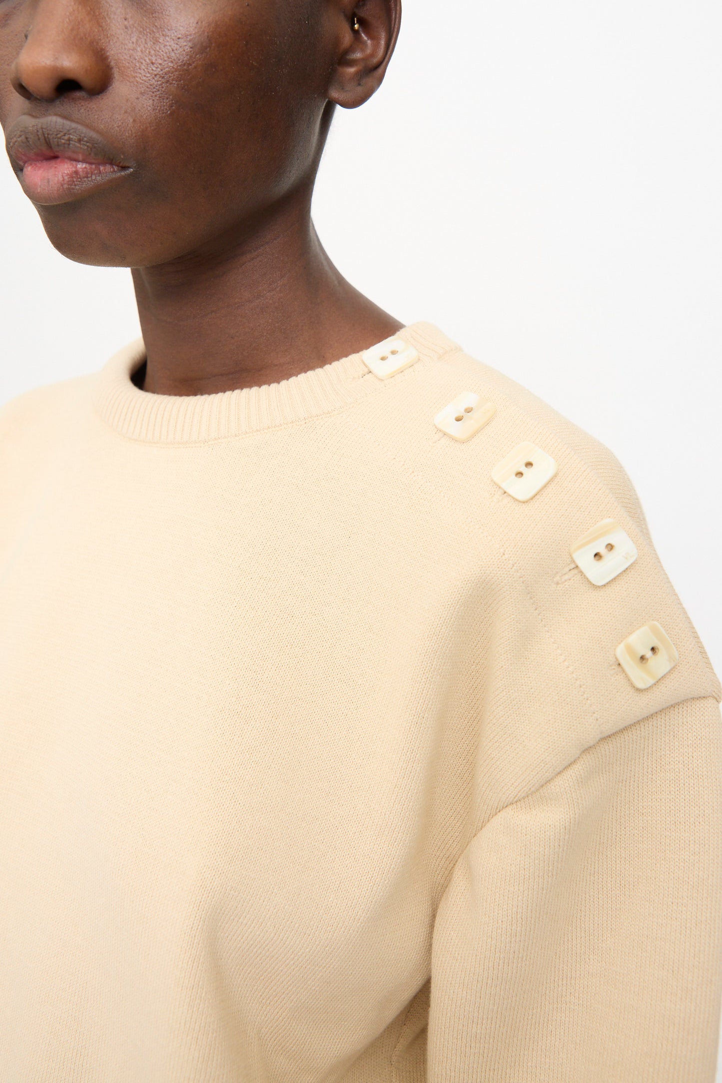 Model wears the Veronique Leroy Button Shoulder Boxy Sweater in Cream, featuring a boxy fit and four square cream buttons on the left shoulder, shown from the chest up against a plain background.