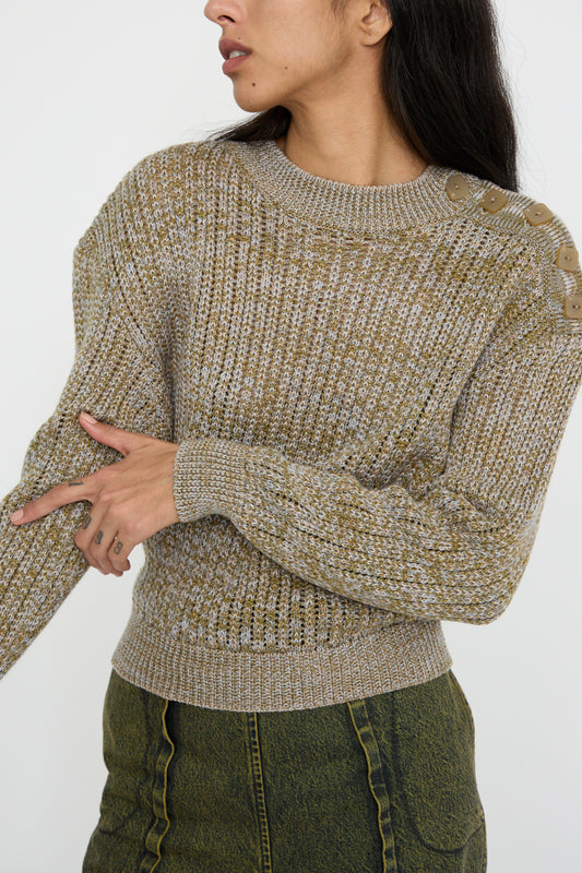 A person is wearing Veronique Leroy's Button Shoulder Sweater in Meadown, characterized by a boxy fit and button details on the shoulder, paired with green pants. 