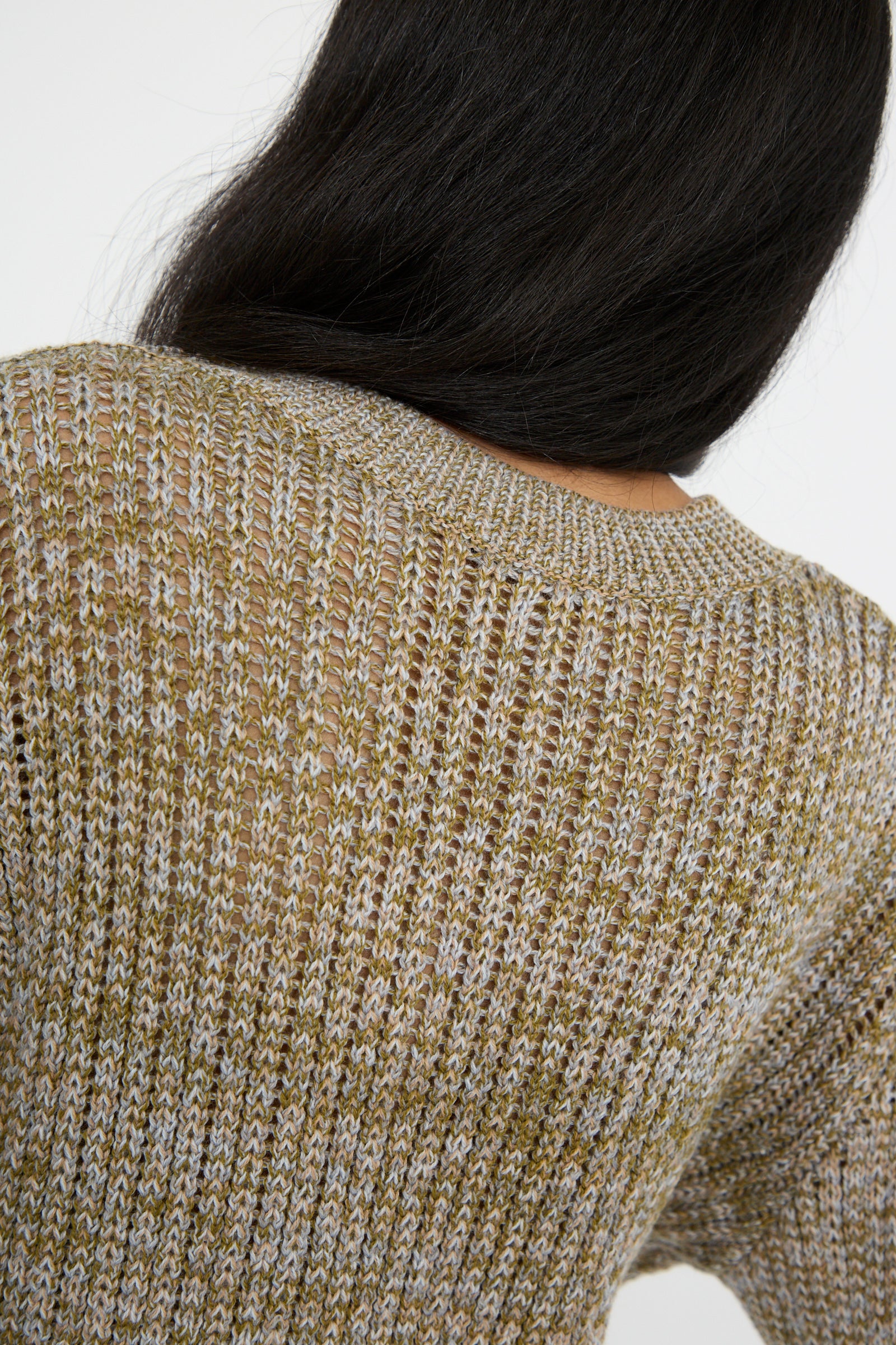 A person viewed from the back with long dark hair is wearing the Button Shoulder Sweater in Meadown by Veronique Leroy, featuring a boxy fit and knit pattern in shades of brown and gray. 