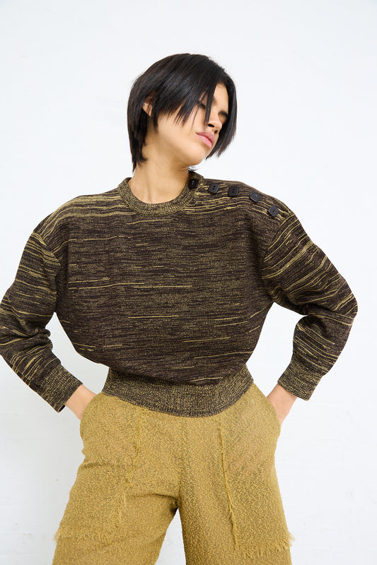 A person with short black hair wearing a Veronique Leroy Cotton Boxy Sweater in Pepper, textured brown top and yellow pants, posing with hands on hips against a white background.