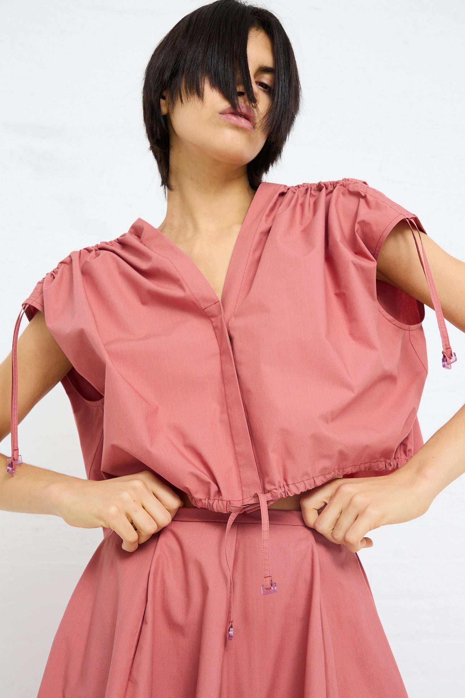 Woman in a pink Veronique Leroy Cotton Poplin Gathered Top in Canyon with adjustable ruche details, posing with hands on hips.