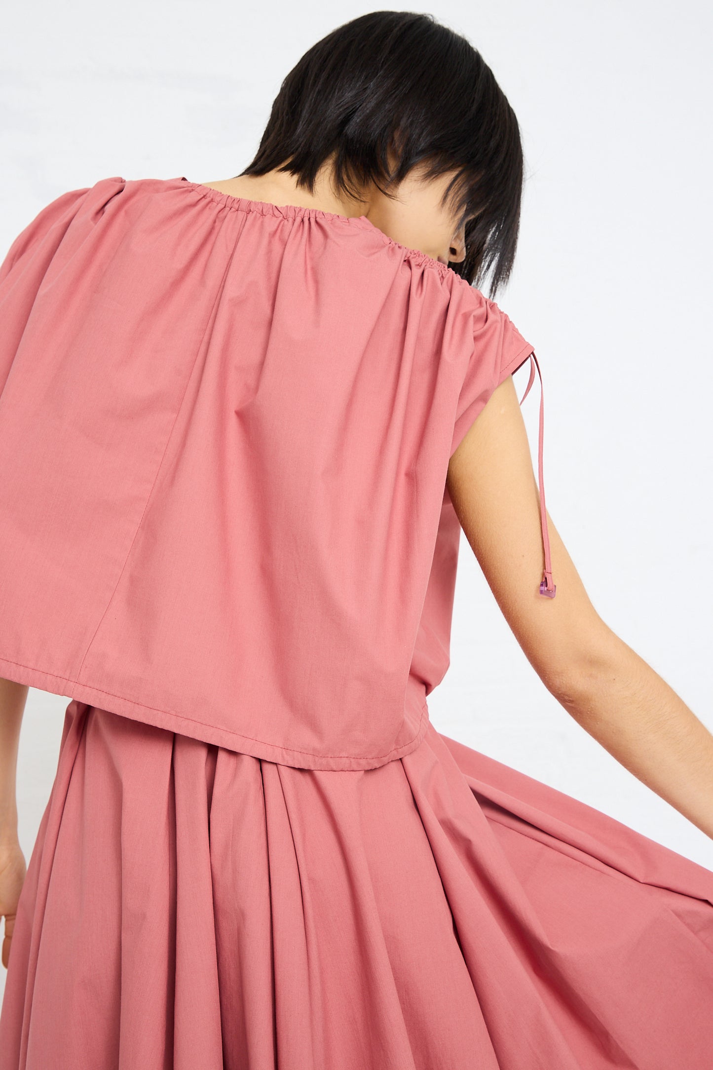 Woman in a pink dress with a Cotton Poplin Gathered Top in Canyon by Veronique Leroy and an adjustable ruche detail.