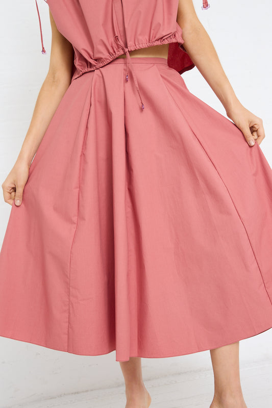 Woman showcasing the flare of a coral pink midi dress with a pleated Cotton Poplin Skirt in Canyon by Veronique Leroy.