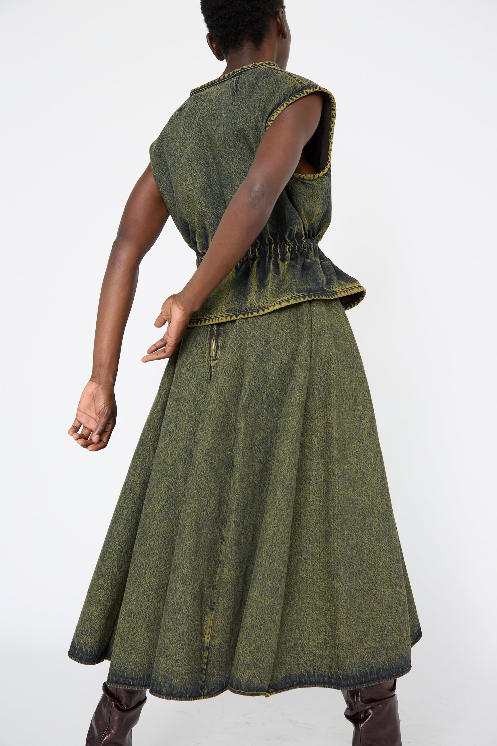 A person is wearing the Veronique Leroy Denim Skirt in a cumin shade, made from 100% cotton, with a high waist and an ankle-length design, standing against a white background.