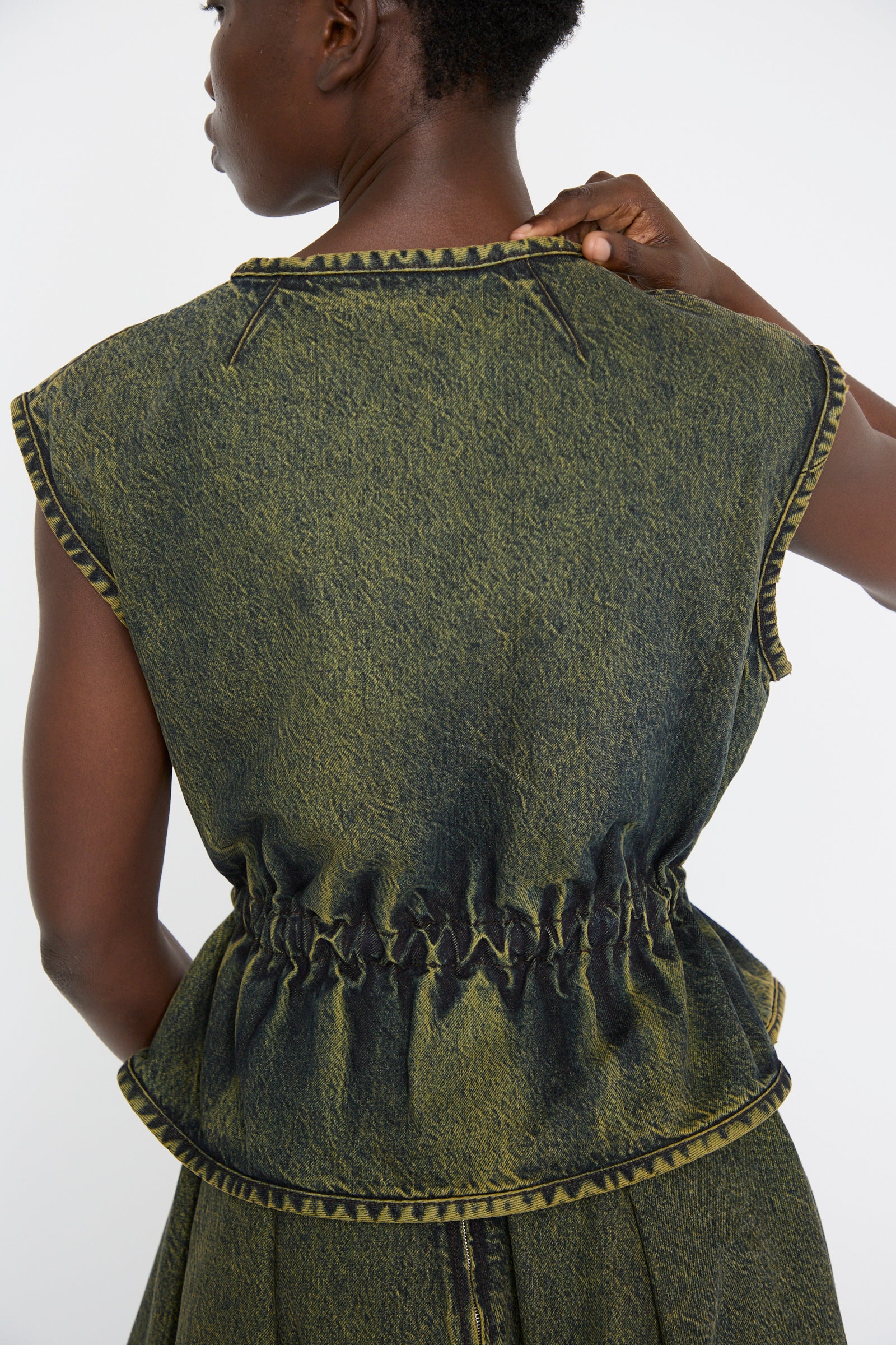 The individual wearing a sleeveless, vest in a cumin color with a cinched waist in cotton denim.