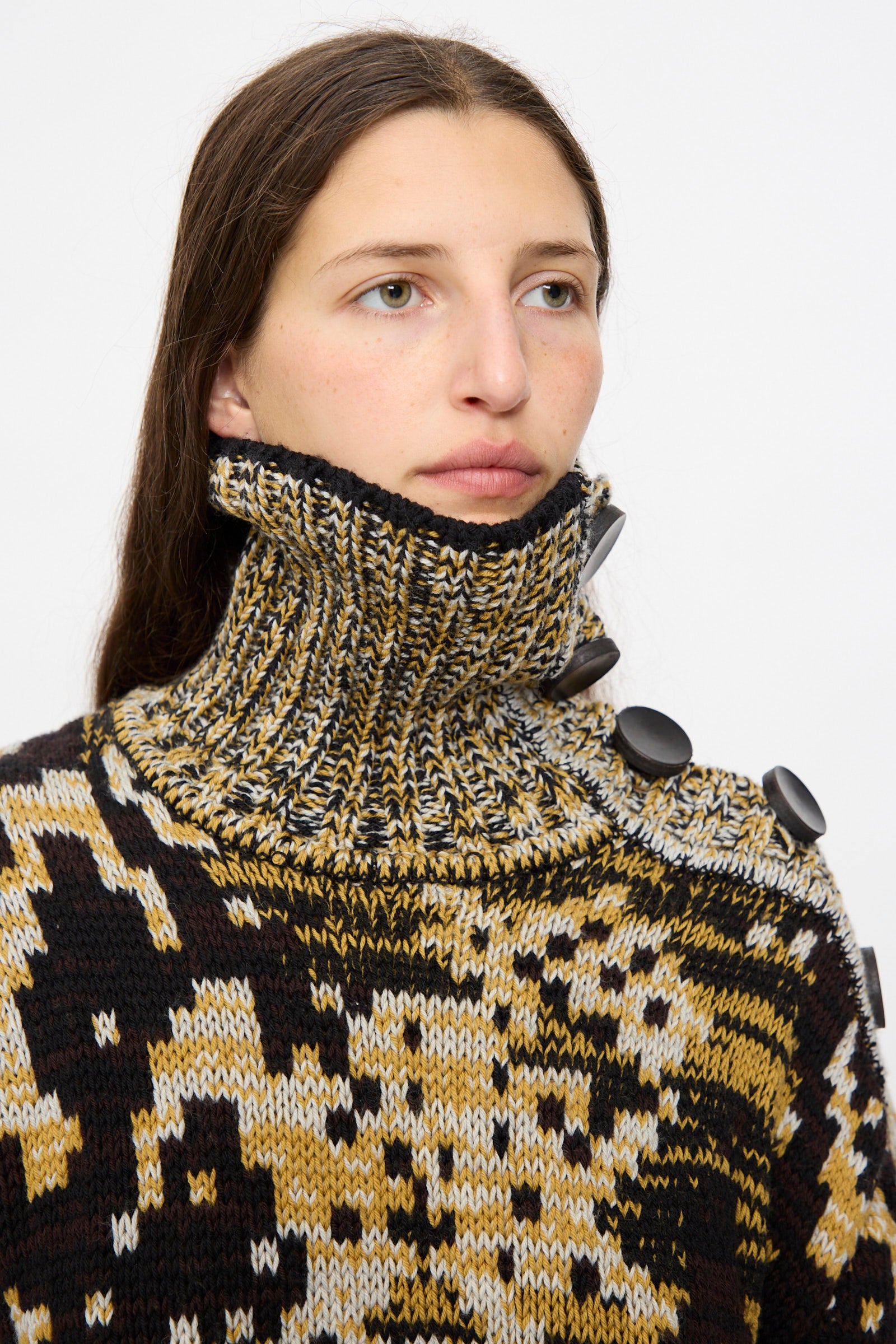 A person with long brown hair wears the Veronique Leroy Sweater in Sepia, a high-neck, relaxed-fit graphic knit with large black buttons on the collar and shoulder.